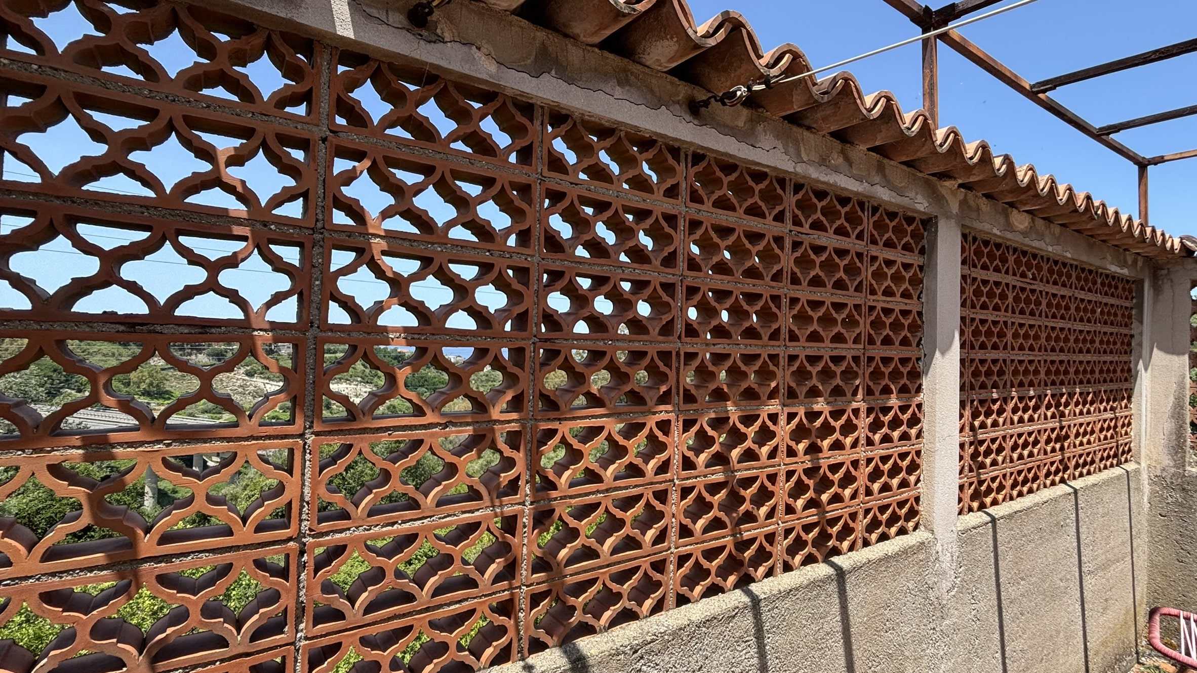 Barriera in mattoni forati rossi per recinzione o privacy di un edificio. Muratura decorativa e di sicurezza, ideale per esterni, con vista sul paesaggio verde e azzurro del cielo.