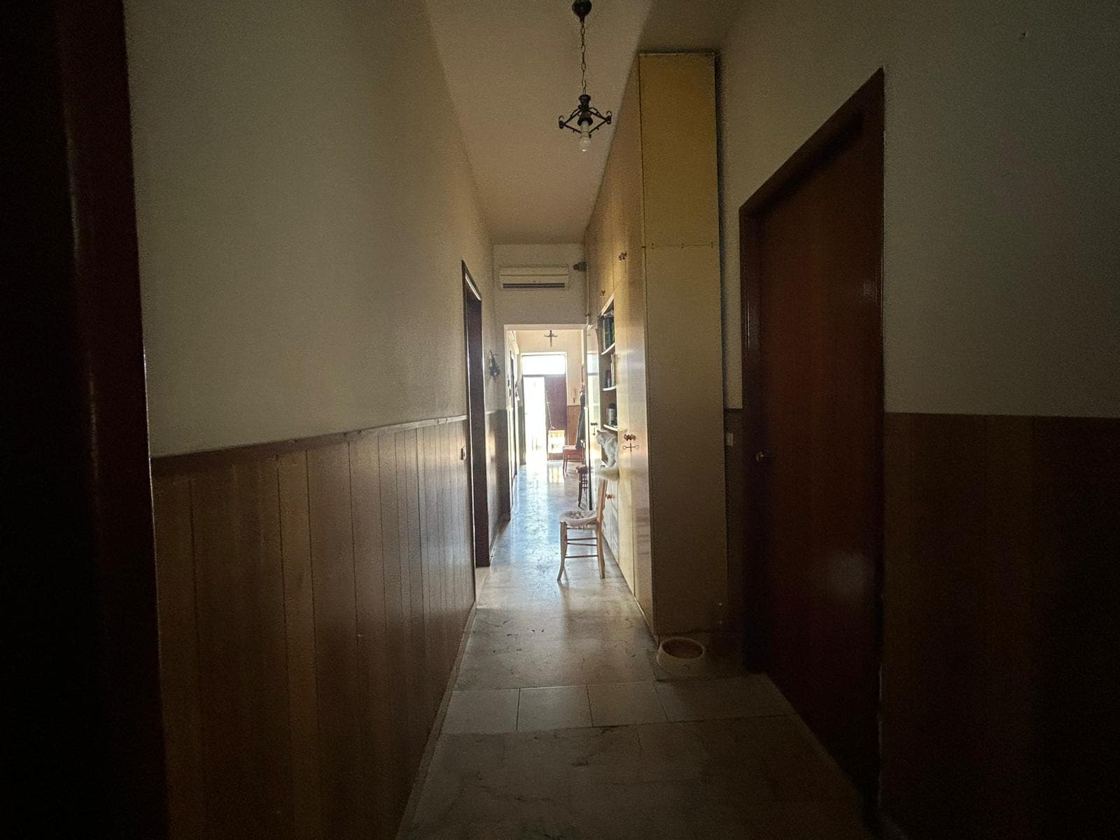 Scorcio di corridoio in casa con pareti chiare, rivestimento in legno e porta arancione, vista verso un'area luminosa con mobili e dettagli interni, ideale per affitto o vendita immobili con NextCasa.