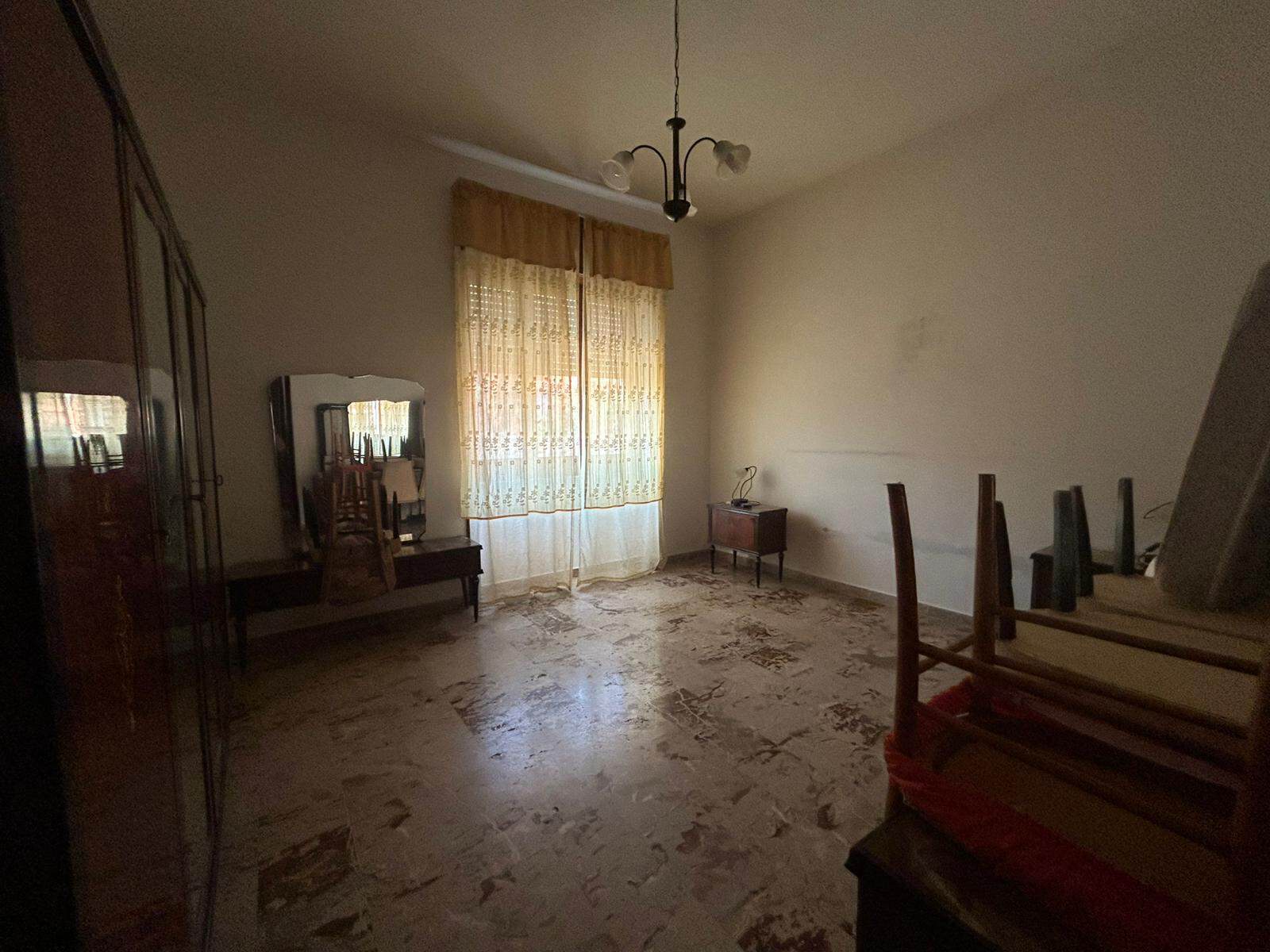 Spazio abitativo con finestra, tende in pizzo e arredi classici, arredamento vintage, pavimento in marmo, ideale per affitti residenziali o vendita immobili di pregio.
