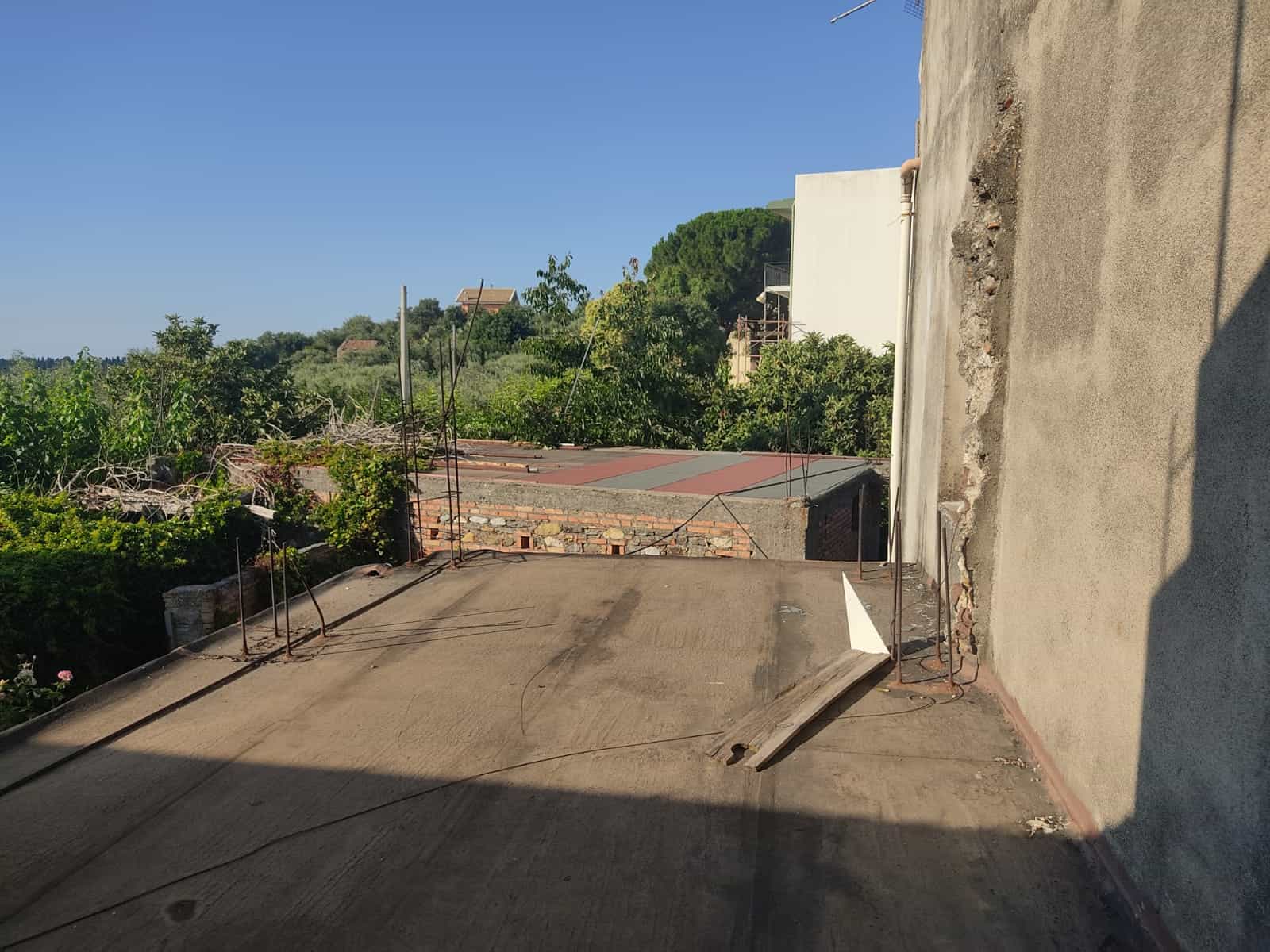 Finestra di un edificio in fase di ristrutturazione con vista sul verde circostante, tempo soleggiato e cielo blu.