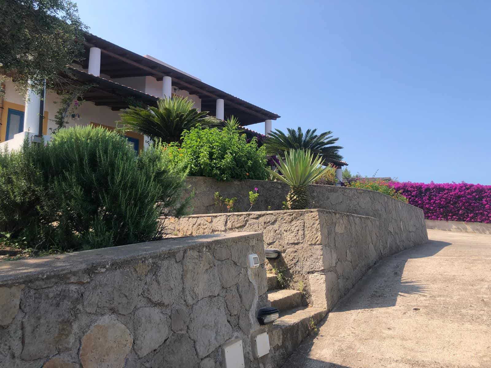 Elegante casa di campagna con terrazza e giardino ben curato, circondata da piante tropicali e fiori colorati, ideale per relax e convivialità in vendita o affitto.
