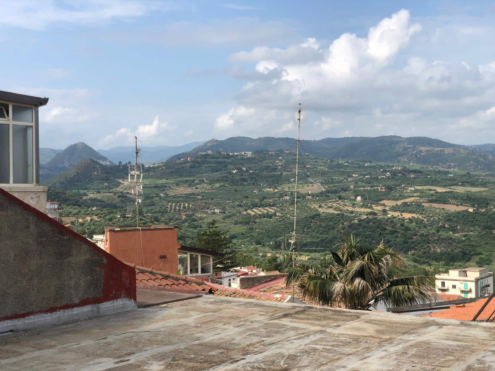 Vista panoramica delle colline e delle montagne dall'area di un terrazzo in una zona residenziale, con tetto in piastrelle e edifici circostanti, perfetta per immobili e immobiliari.