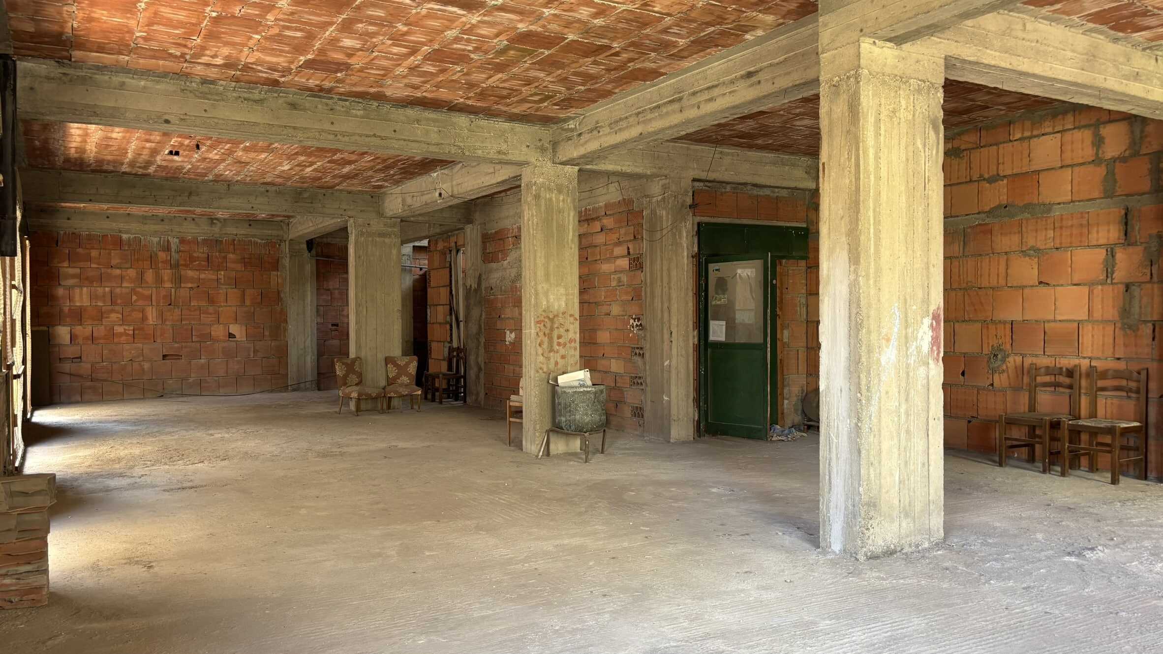 Un ambiente spazioso in fase di ristrutturazione con mattoni a vista, colonne in cemento e pavimento in calcestruzzo, pronto per essere trasformato in una casa moderna o commerciale.