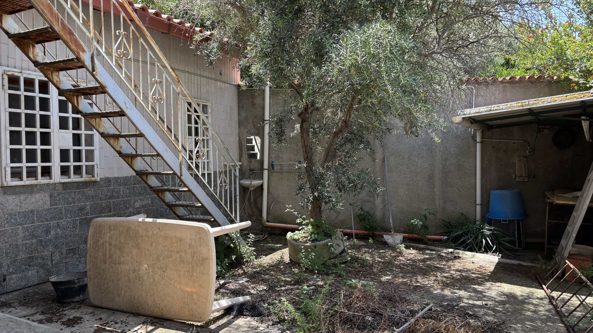 Vecchia scala in ferro arrugginita e cortile con piante verdeggianti, ambiente esterno di casa, con lavabo in pietra e arredi da giardino, zona relax all'aperto, contesto rurale ed autentico.
