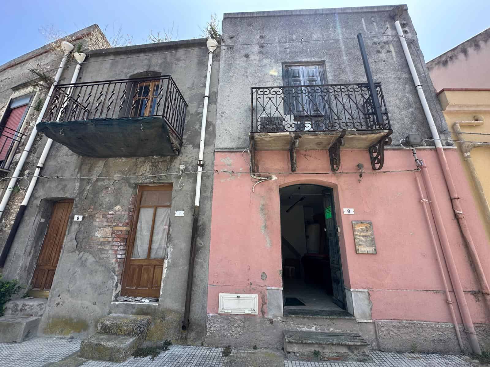 Vecchia casa storica con balcone in ferro battuto, facciata in pietra e porte in legno, tipica architettura italiana, perfetta per restaurare e valorizzare elementi storici e culturali.