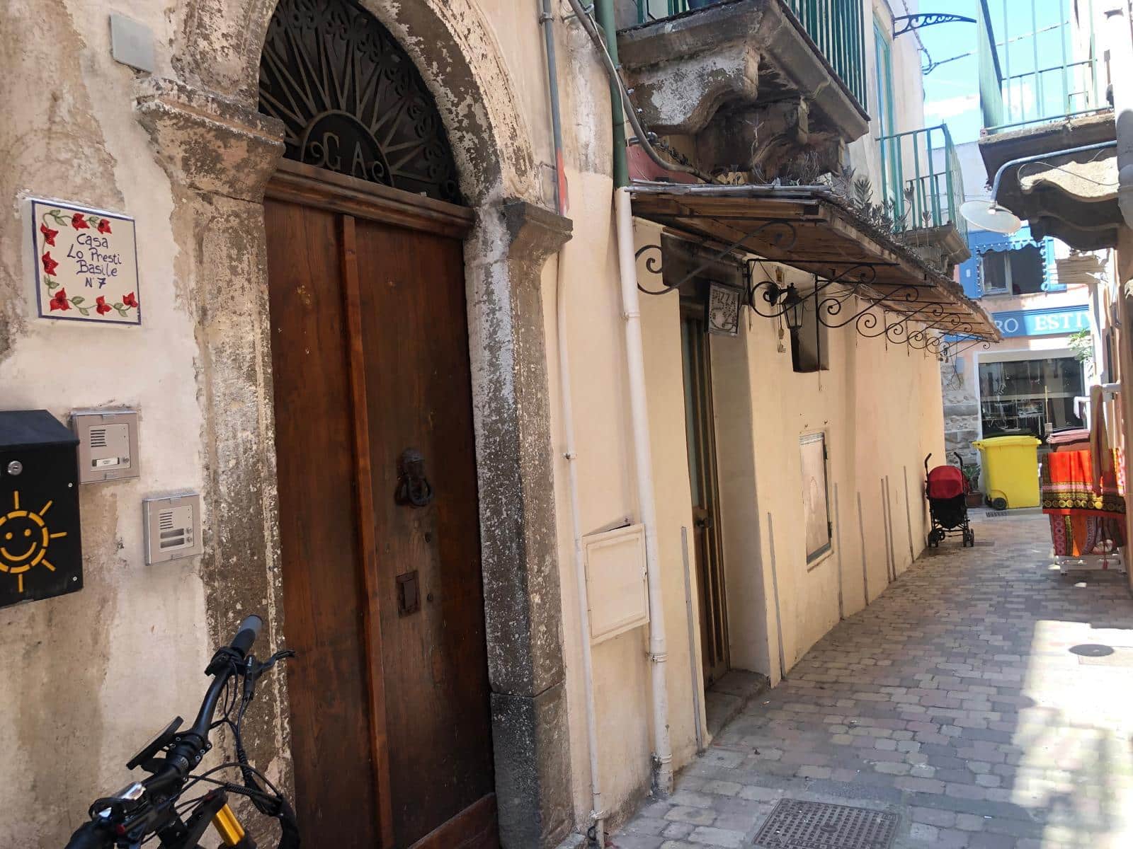 Vecchia porta in legno con architrave in pietra e muro in pietra e intonaco, dettaglio di strada nel centro storico di Lecce, Italia, con bici, casetta delle poste e barriere di sicurezza.
