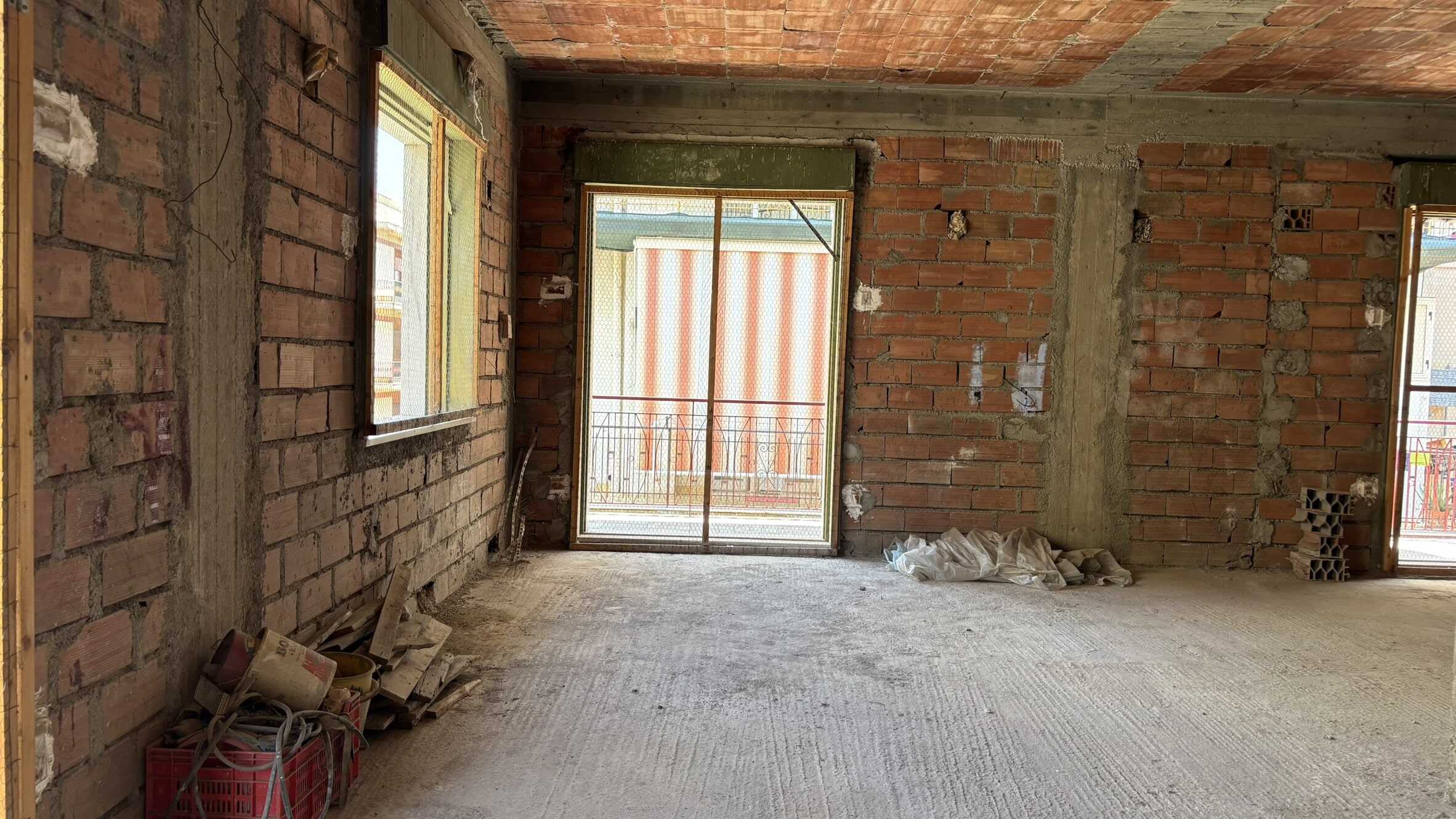 Locale in costruzione con pareti in mattoni e grande porta finestra che dà su un balcone, pronto per essere arredato e personalizzato, ideale per progetti immobiliari e ristrutturazioni.