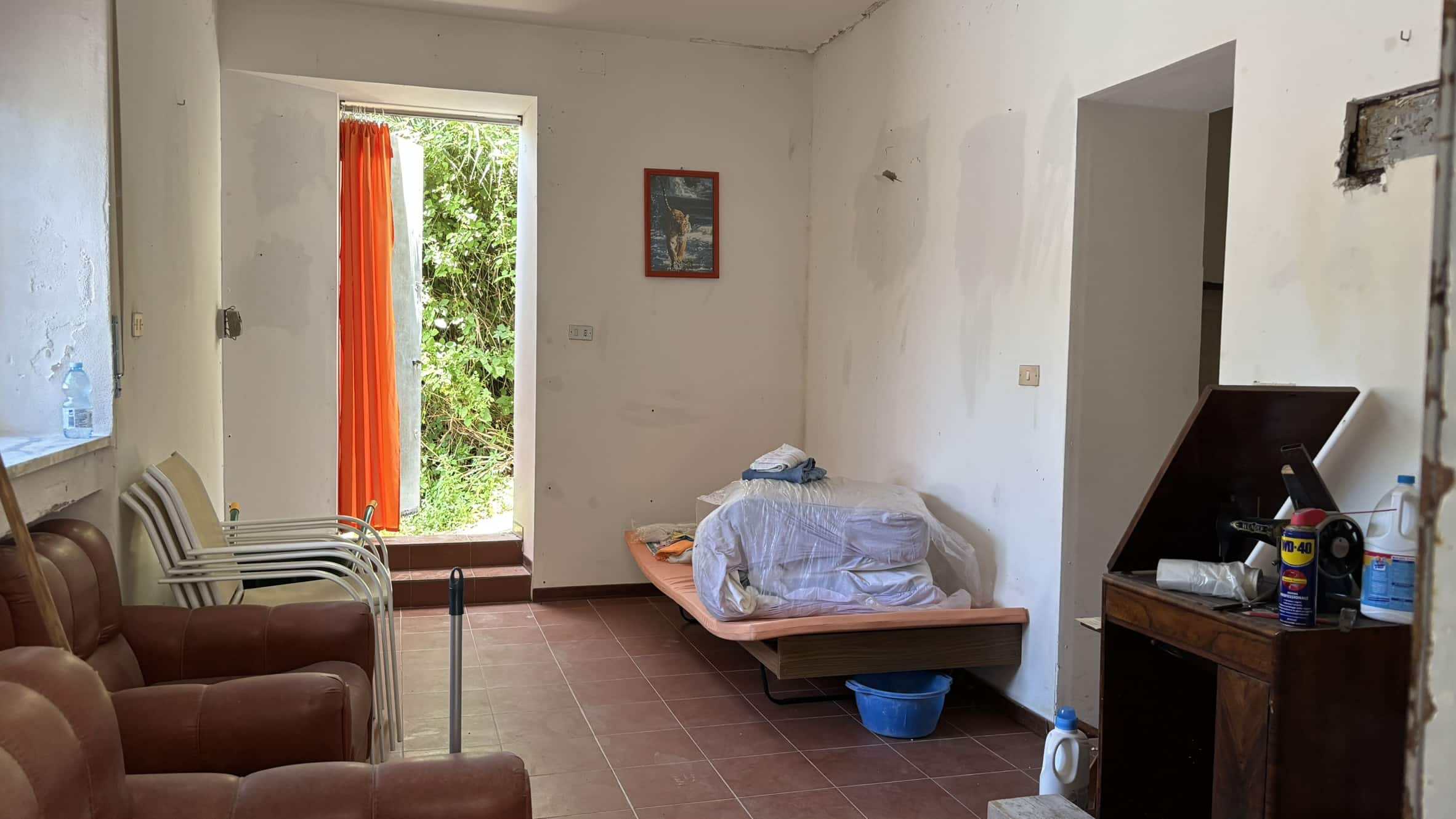 Letto singolo trasformabile in divano in una casa da ristrutturare, mobili e arredamento minimal, finestra con vista sul giardino, dettagli di rinnovamento e rinnovazione edilizia.