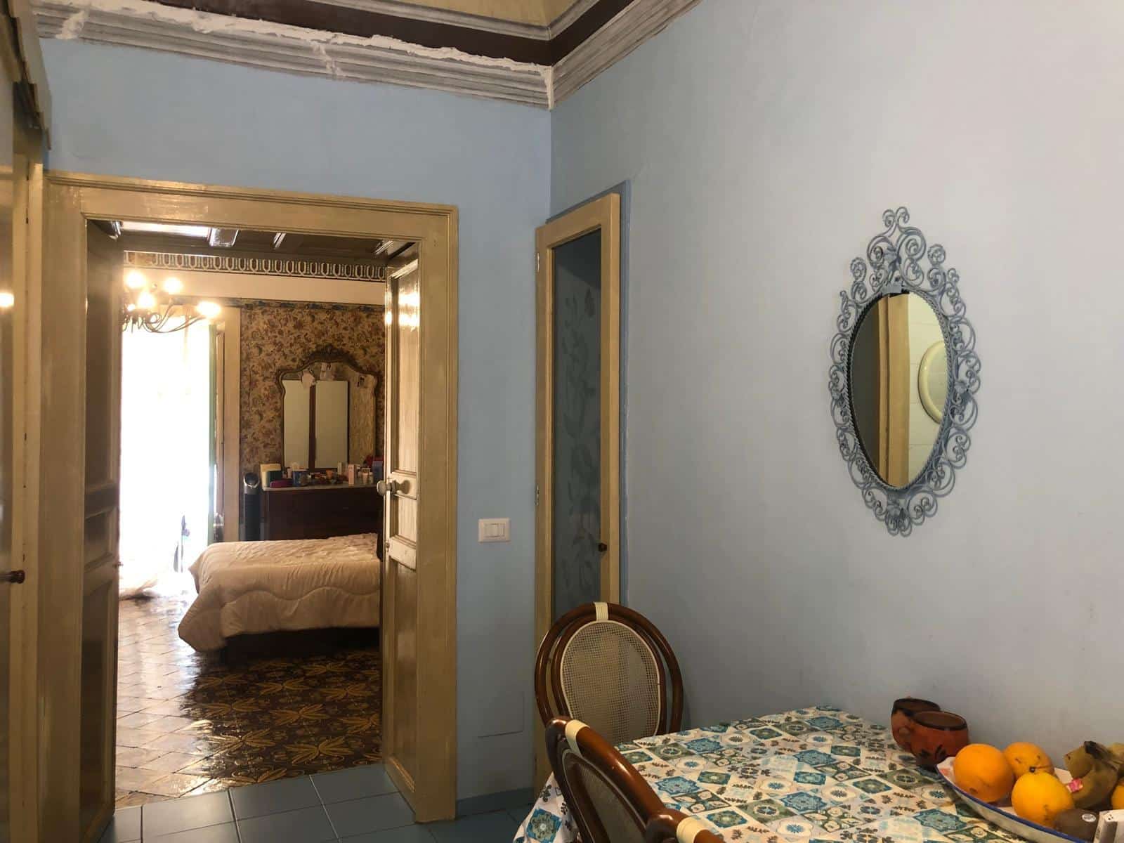 Finestra su una stanza da letto con arredamento classico e pareti dipinte di azzurro, vista attraverso una porta decorativa, con un tavolo apparecchiato e lampadario elegante in stile vintage.