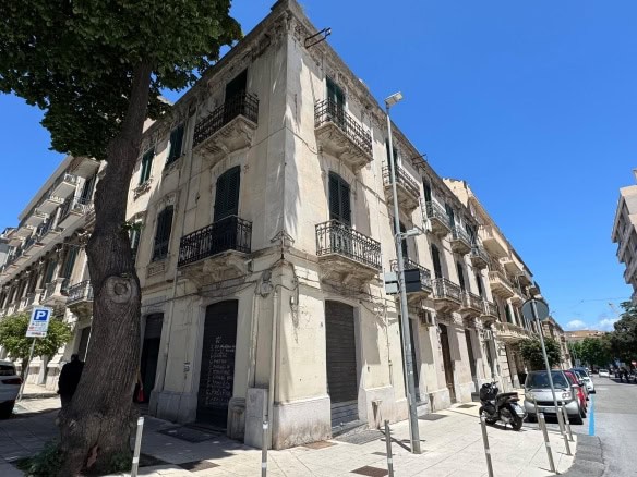 Storica palazzina residenziale in centro città, edificio con affacci su strada principale, con balconi in ferro battuto, finestrature con persiane e pareti in pietra chiara, in zona urbana di Napoli.