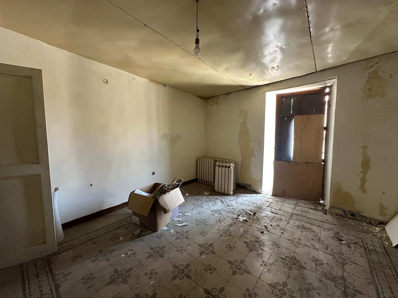Soggiorno da ristrutturare, con pareti sbiadite e pavimento antico, ideale per chi cerca una casa da personalizzare in modo unico e funzionale.