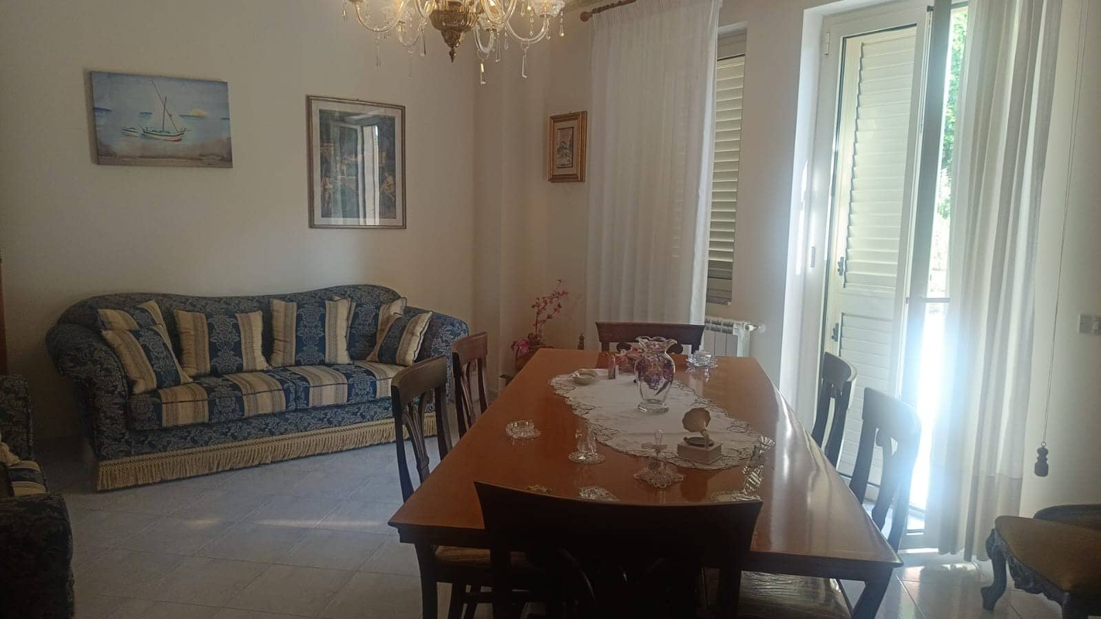 Comfortabile soggiorno con divano classico e tavolo da pranzo elegante, luminoso con grande finestra e tende, arredamento in stile tradizionale, decorazioni floreali, ambienti accoglienti e ben illuminati, ideale per case in vendita o affitto a NextCasa.