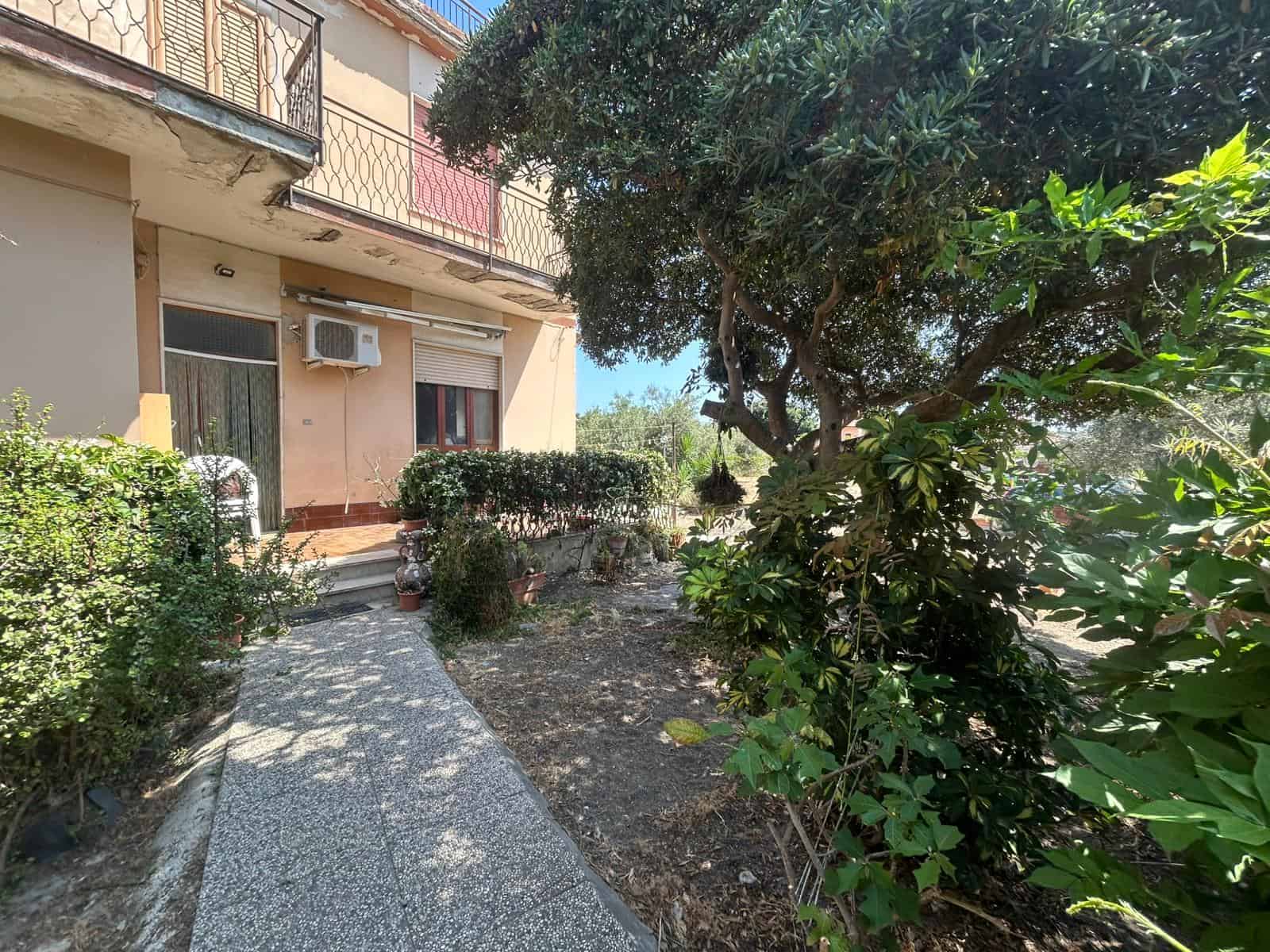 Veranda esterna con giardino e piante decorative, ideale per case in vendita o affitto, immersa nel verde, luminosa e accogliente in zona residenziale.