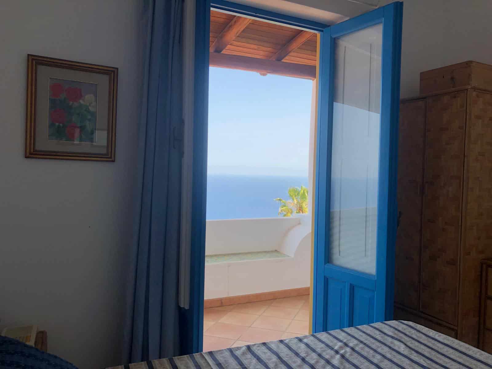 Vista mare dalla camera con balcone, infisso blu e arredo in stile classico, ideale per case vacanza e immobili di lusso.