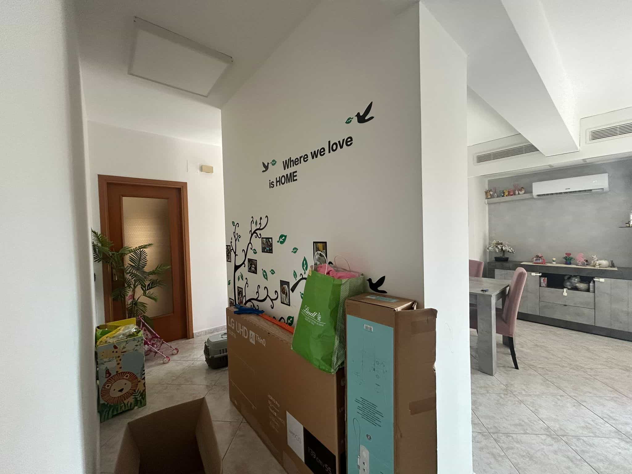 Casina moderna con parete decorativa con scritta "Where we love is HOME" e decorazioni di uccelli. Interno luminoso e accogliente con zona pranzo e ingresso.