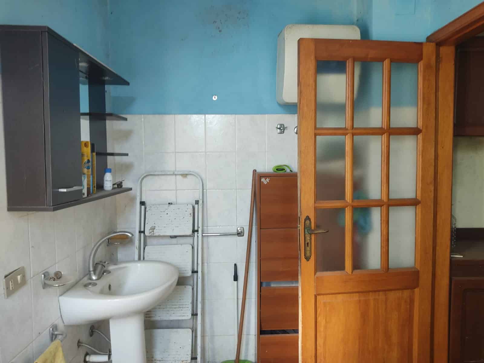 Stanza con porta in legno con vetri, lavabo e scaffale, ideale per ambienti domestici, con pareti blu e piastrelle bianche, ambientazione semplice e funzionale.