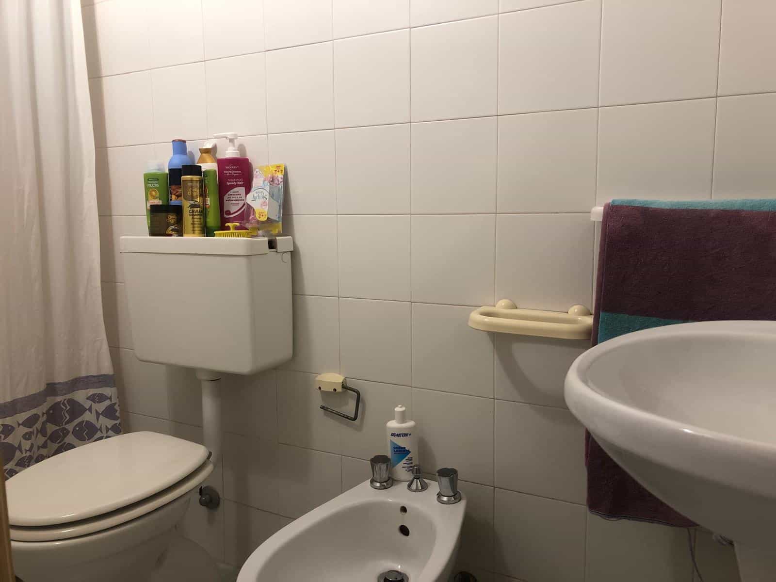 Radiatore di bagno con prodotti per l'igiene e asciugamani colorati, box doccia, sanitari e parete in piastrelle bianche, ambiente funzionale e ben curato per appartamenti in vendita o affitto.