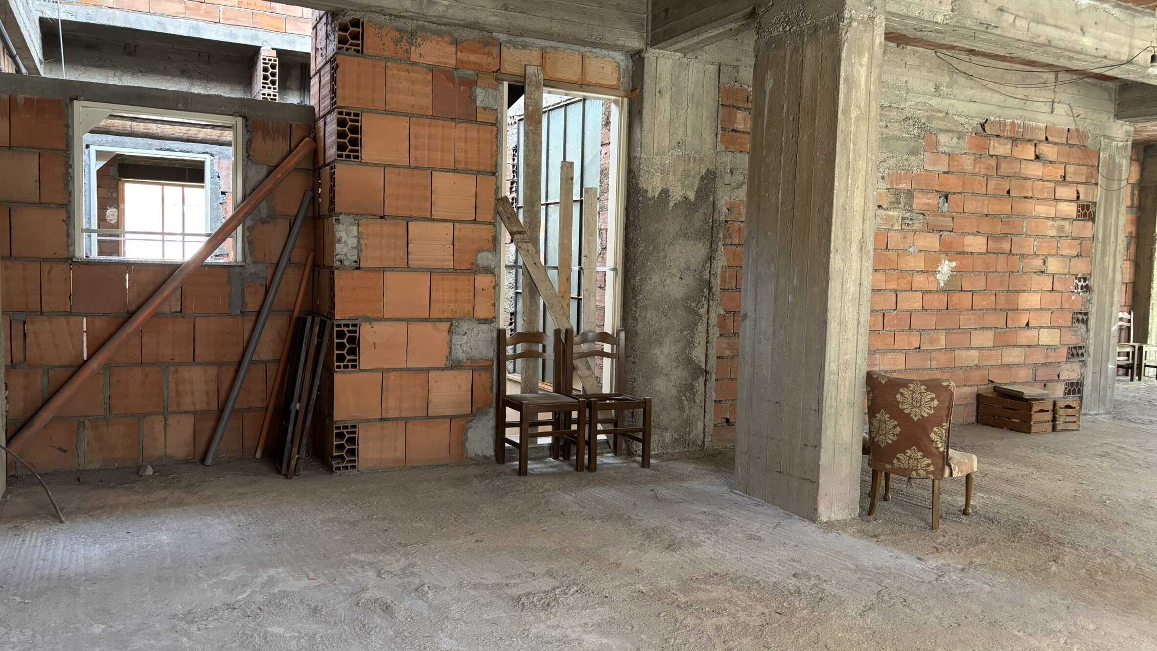 - Muri in mattoni rossi in costruzione, interni di una casa ancora in fase di sviluppo, struttura edilizia visibile, materiali da costruzione e arredi di recupero presenti.