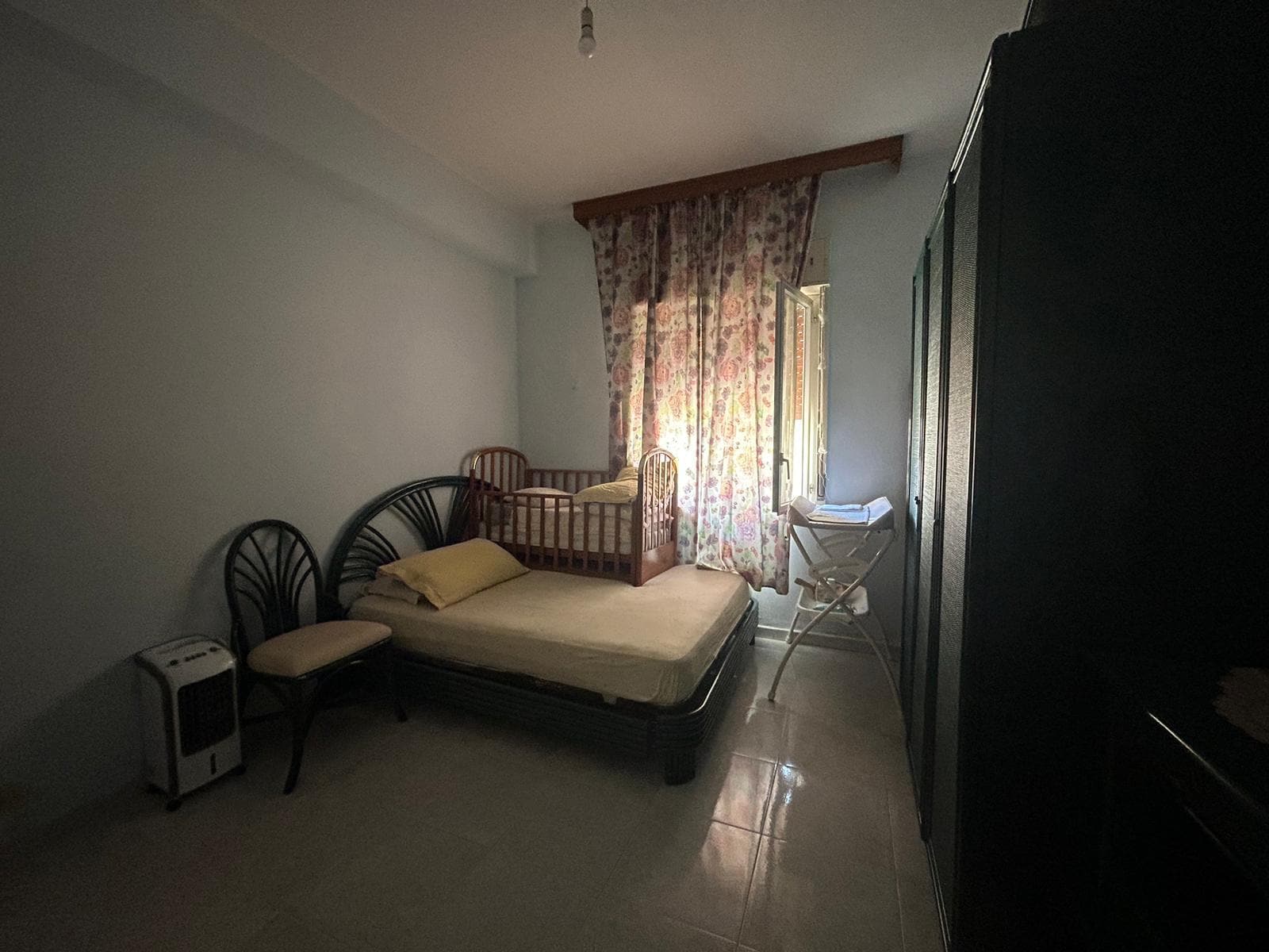 Letto matrimoniale con culla e tende floreali in camera da letto. Mobliari essenziali, ambiente luminoso e accogliente. Ideale per affitto o acquisto di immobili residenziali.