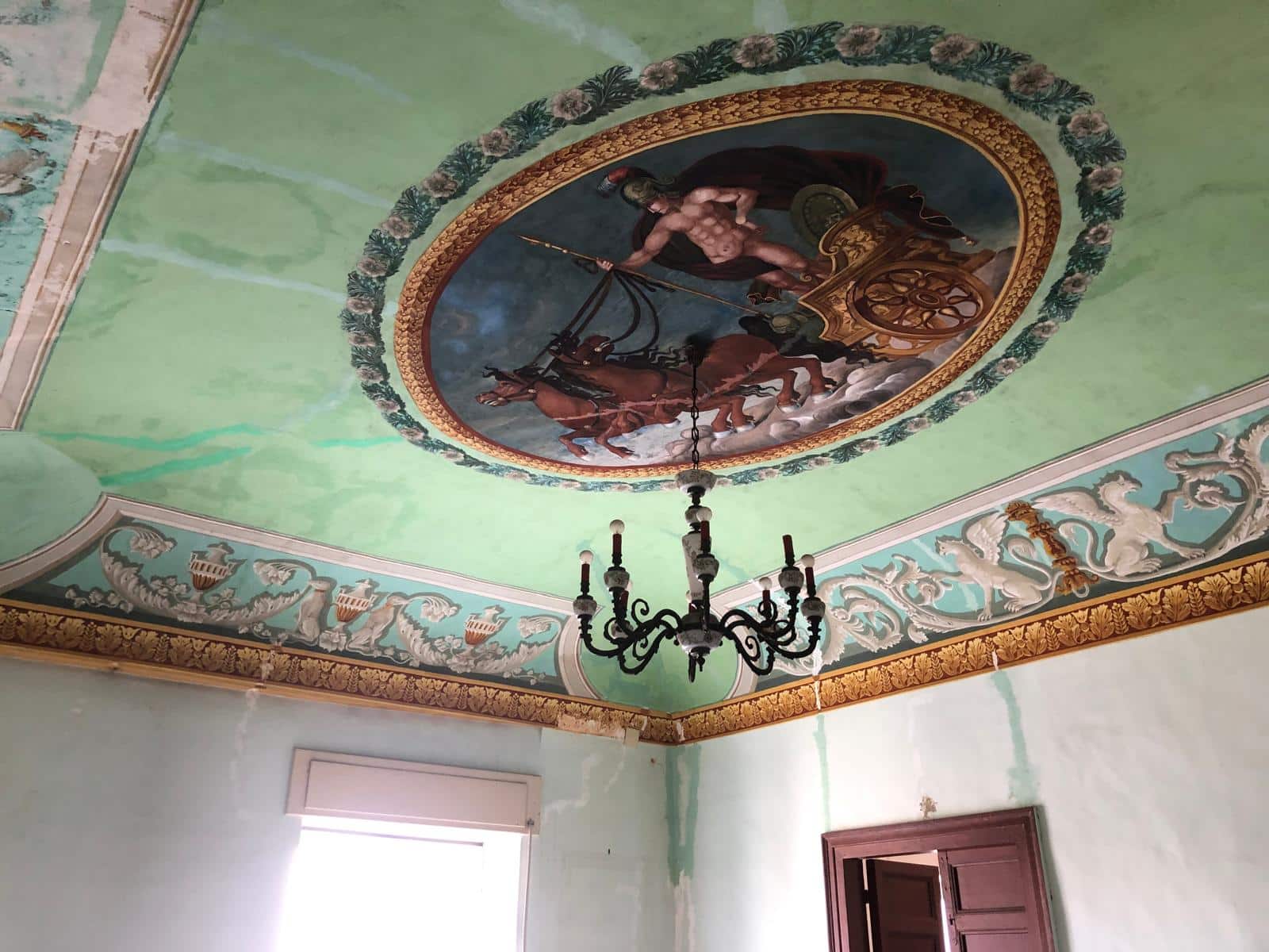 Finestra decorativa sul soffitto storico con affresco e lampadario elegante, in un ambiente di prestigio, ristrutturato con cura, ideale per valorizzare gli interni di un edificio di lusso.