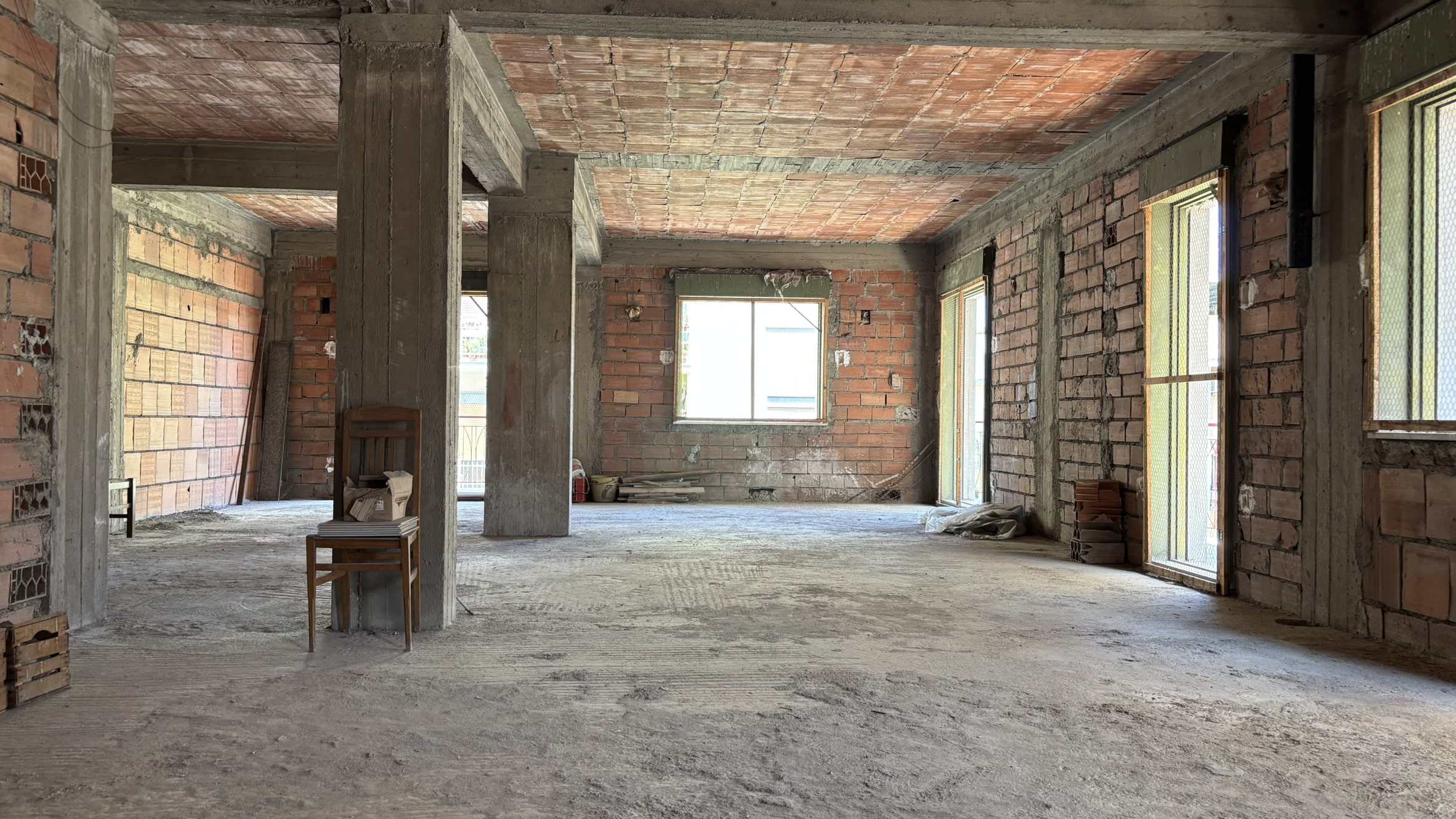 Immagine di un interno di casa in costruzione con pareti in mattoni a vista e strutture in cemento, pronta per essere rifinita e arredata.