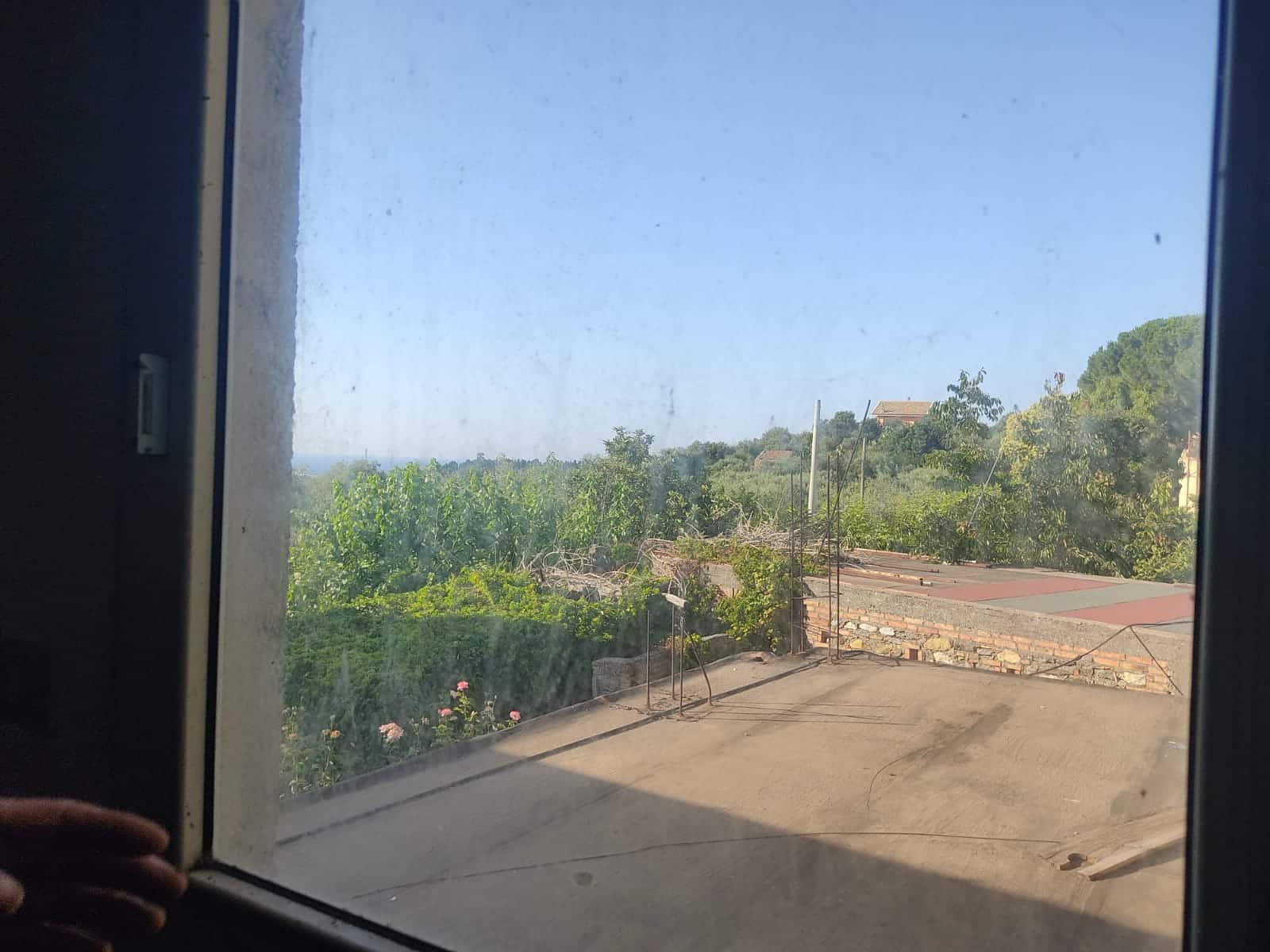Su vista da una finestra con paesaggio rurale, colline e vegetazione, luminoso e tranquillo.