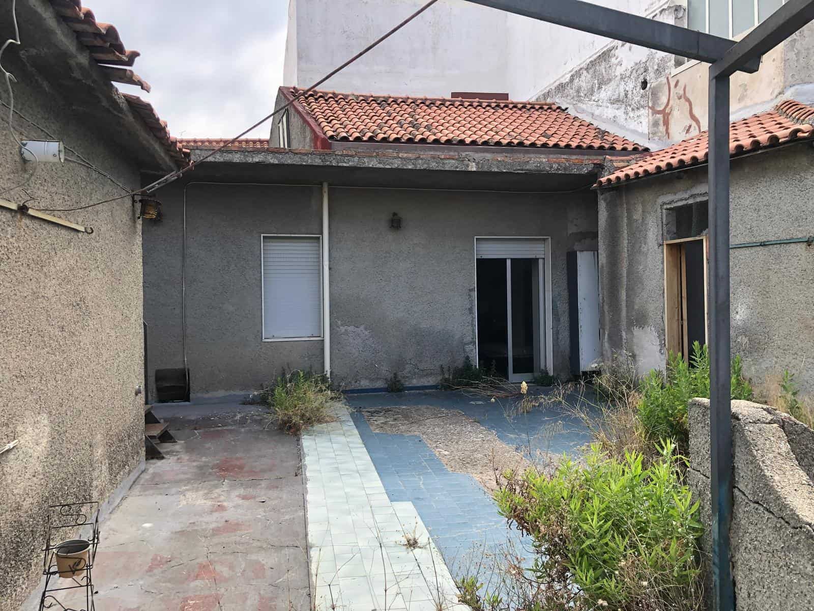 Veranda esterna di casa in stile rustico con piastrelle usurate, piante selvatiche e strutture di sostegno in metallo, atmosfera di ristrutturazione in corso, contesto di cortile o giardino privato.