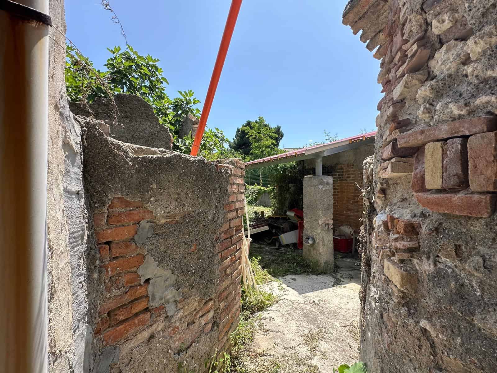 Vecchio muro di pietra e mattoni in un cortile con vegetazione e cielo azzurro, stile rustico, immobile da ristrutturare, atmosfera autentica, progetto di restauro, abitazione di charme.