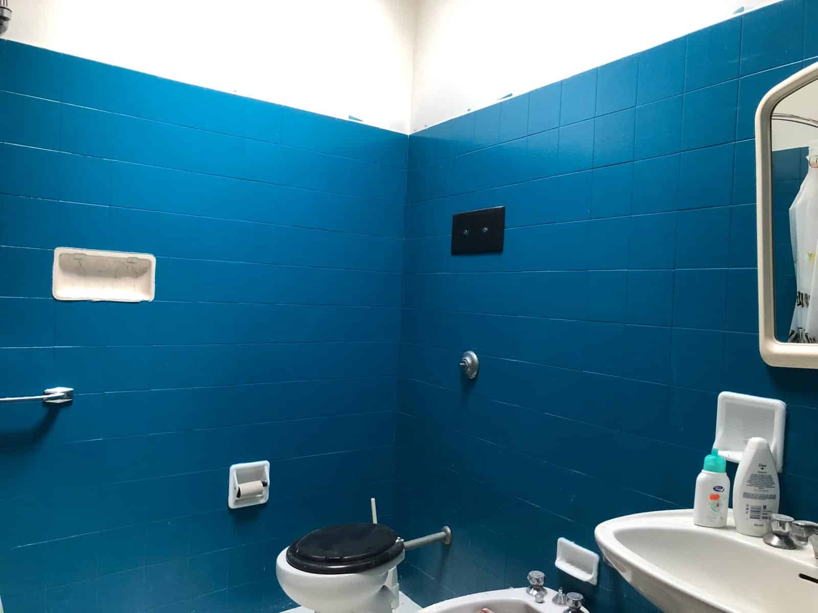 Azzurro bagno con pareti rivestite di piastrelle blu, servizi igienici e lavabo, specchiera e accessori bagno, ambiente funzionale e moderno, ideale per spazi small o ristrutturazioni casa.