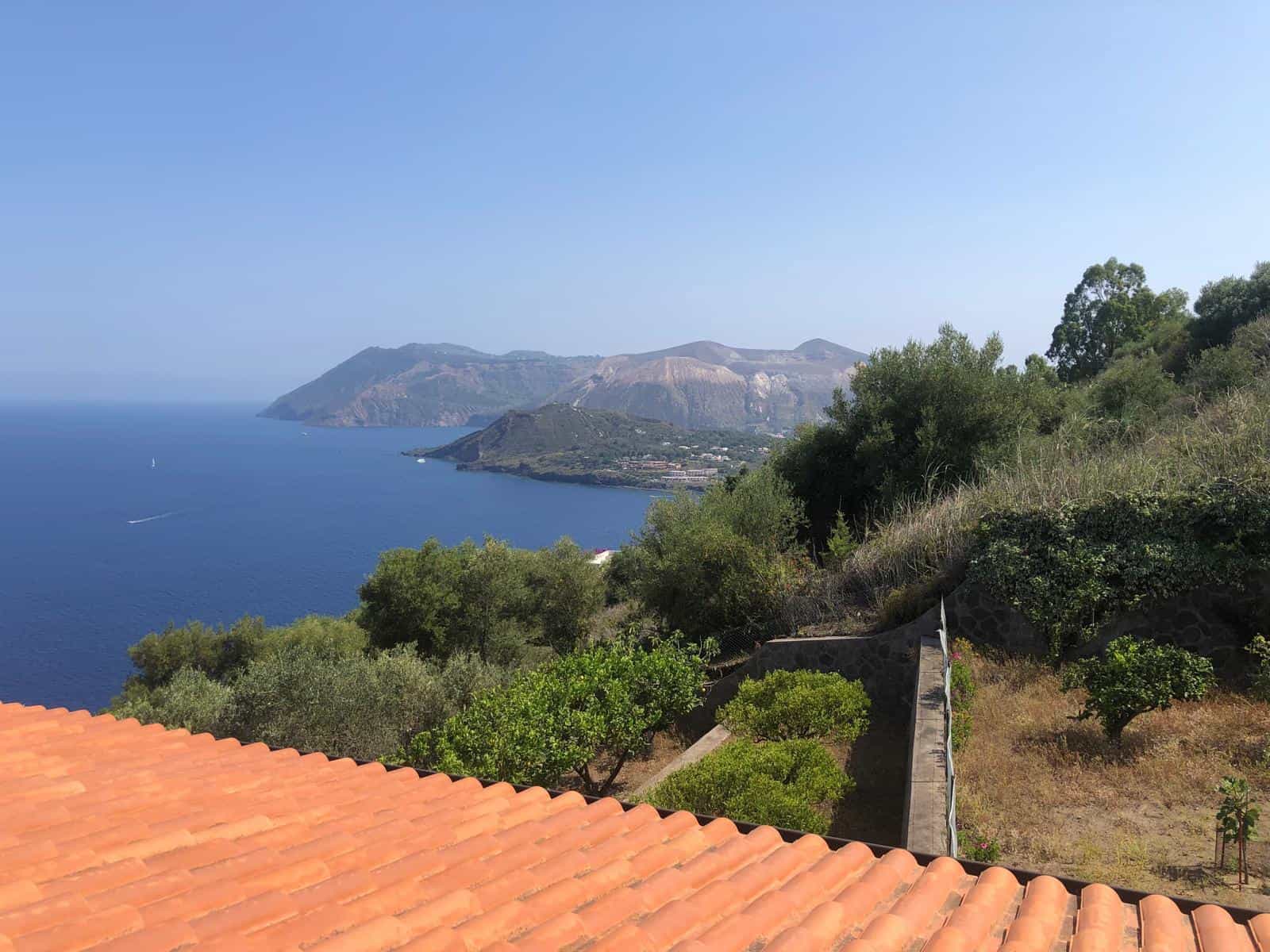 Vista panoramica della costa di Capri con mare blu, montagne e verdeggianti pendii, stabile sul tetto di tegole arancioni. Perfetta per case vacanza di lusso e immobili sul mare.