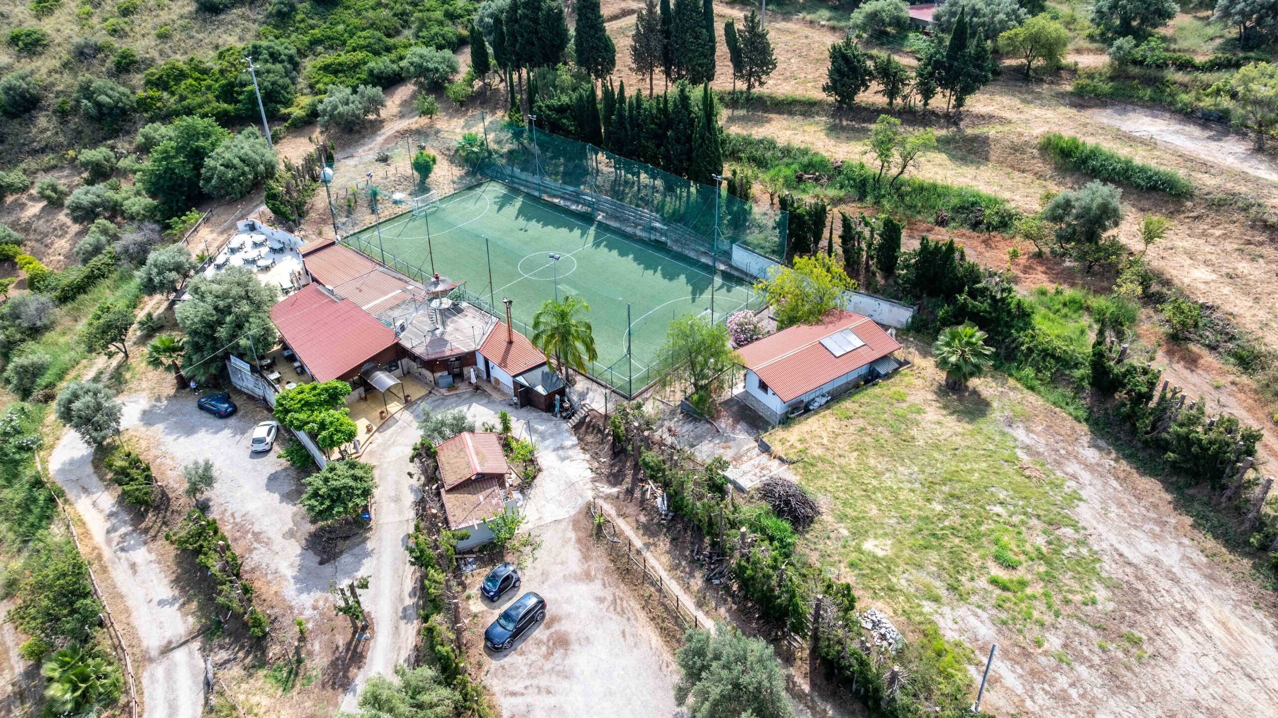 Ampia veduta aerea di una proprietà rurale con campo da calcio, zone verdi e strutture ricreative, immersa nella natura toscana, ideale per investimenti immobiliari e case vacanze.
