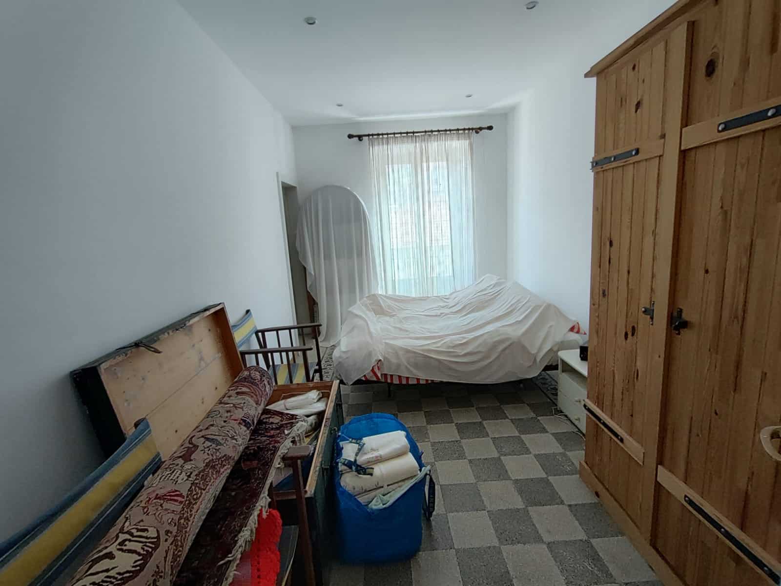 Vestibilità di camera da letto con arredi di legno, letto non rifinito, finestra con tende leggere, armadio in legno, e oggetti vari, esempio di immobile in vendita o in affitto.