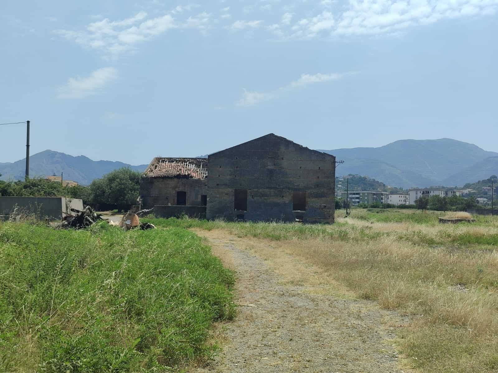 Vecchio fabbricato rustico in pietra su un campo aperto con montagne sullo sfondo, ideale per ristrutturazione o realizzazione di una nuova abitazione.