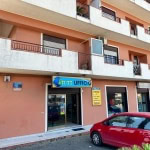 Tutti Ufficio, ufficio commerciale situato al piano terra di un edificio residenziale con facciata color terracotta, con autovettura rossa parcheggiata davanti, segnale commerciale illuminato, in zona urbana.