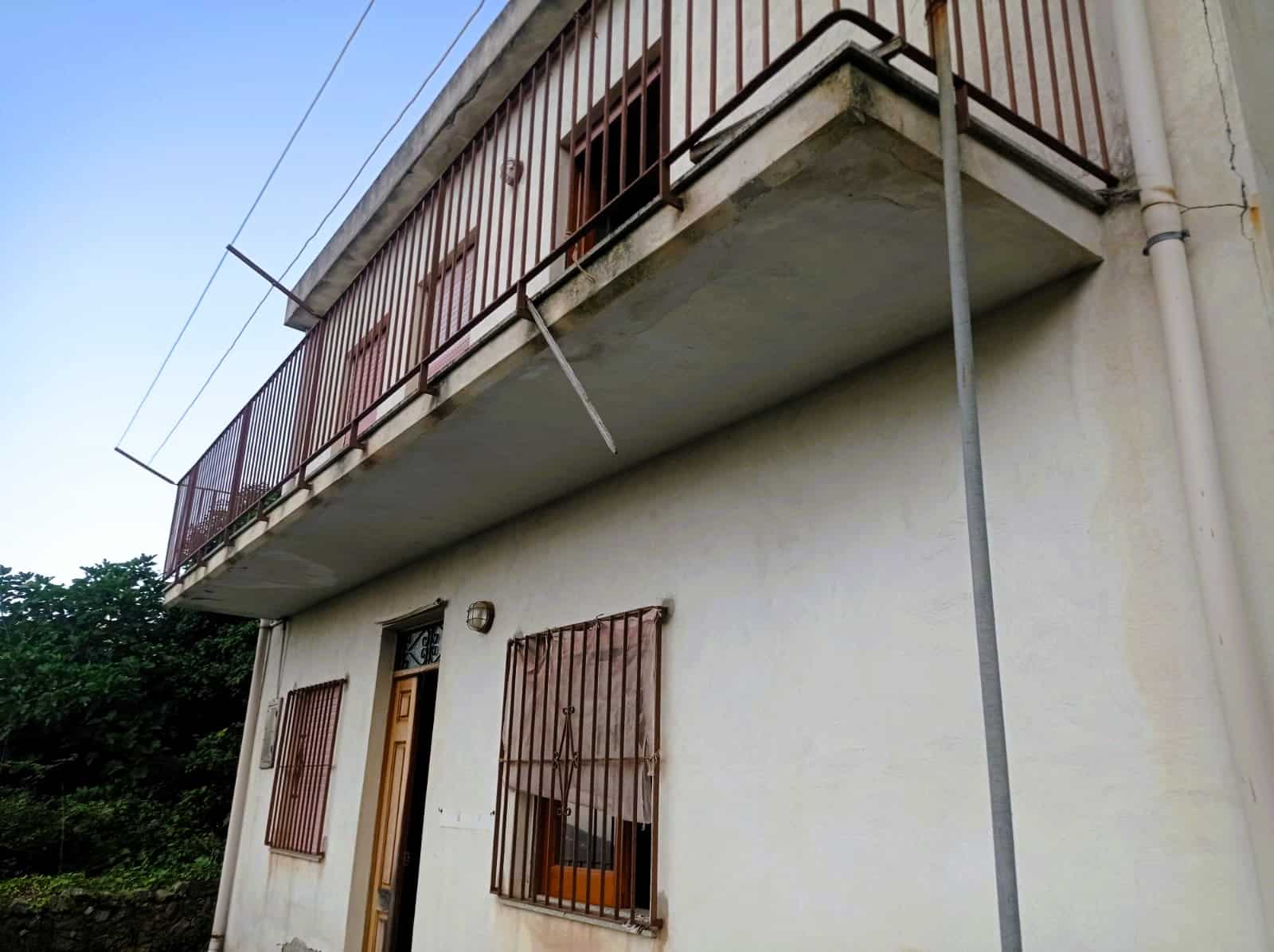 Balcone di una casa con ringhiera in metallo e finestre con inferriate, vista dal basso con cielo azzurro, evidenziando immobili e servizio di realizzazione di balconi NextCasa.