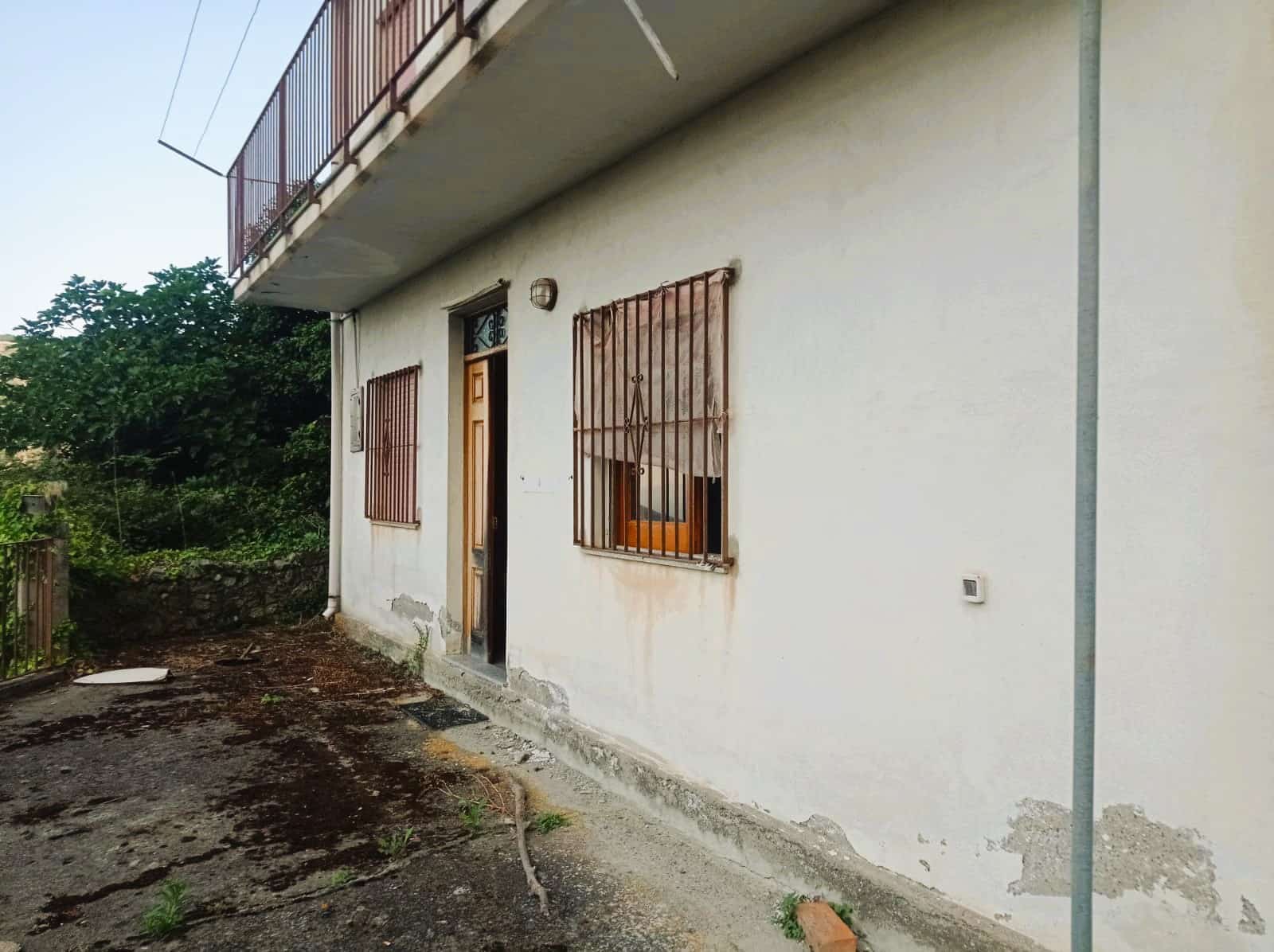 Vecchia casa con finestre in ferro battuto e pareti sbiadite in una zona rurale, pronto per ristrutturazione, immersa nel verde e con un grande potenziale abitativo.