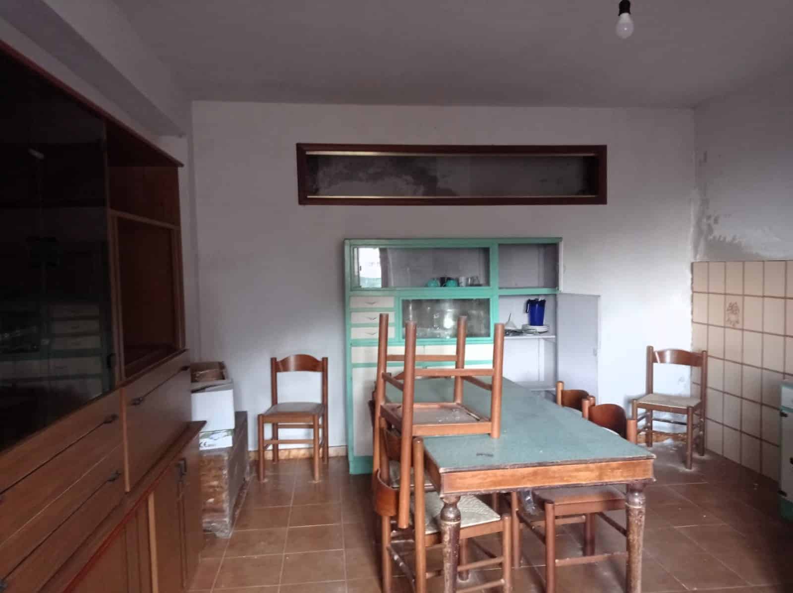 Soggiorno rustico con tavolo da pranzo, sedie in legno, pareti bianche e arredi semplici, stile minimalista e pratico, ambientazione abitativa da rinnovare, atmosfera informale, spazio pronto per ristrutturazione.