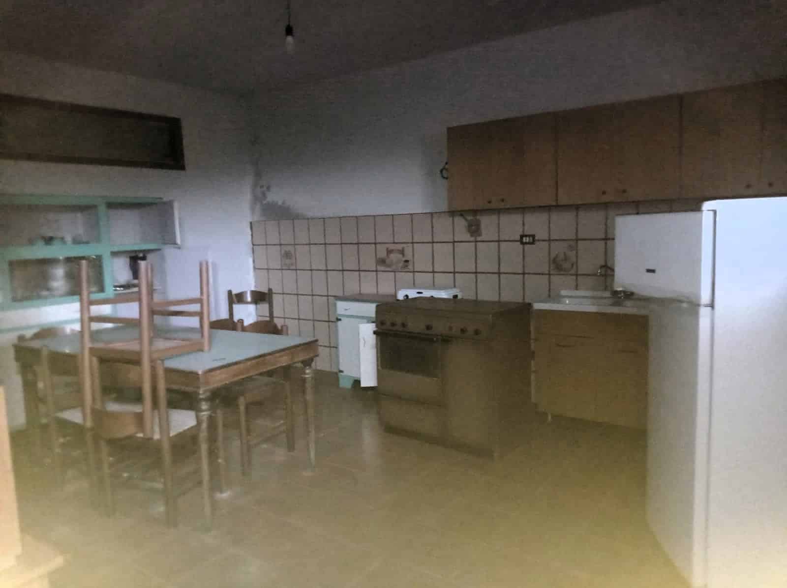 Stanza da cucina con mobili in legno, frigorifero e fornelli, pareti in piastrelle con decorazioni, zona pranzo con tavolo e sedie in legno, ambiente da ristrutturare e arredare.