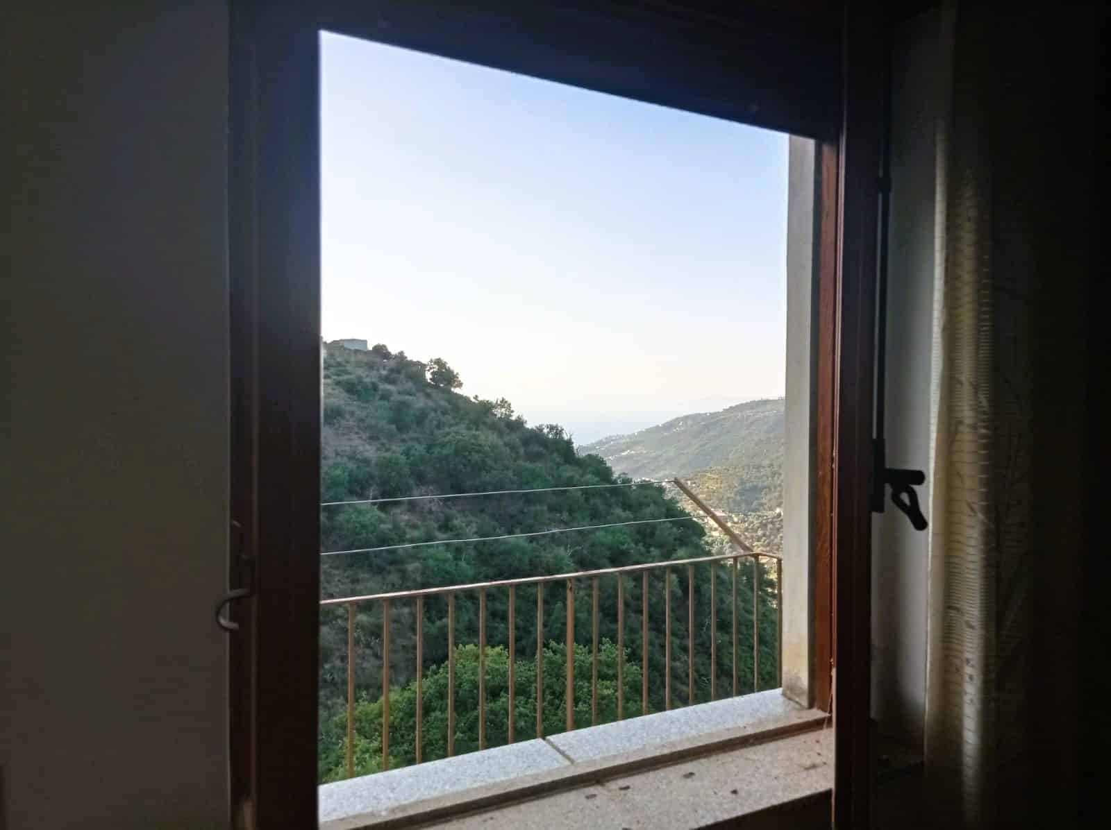 Vista panoramica delle colline verdi attraverso una finestra con apertura a battente, perfetta per case immerse nella natura e con viste suggestive, ideale per annunci immobiliari e appartamenti in vendita o affitto.