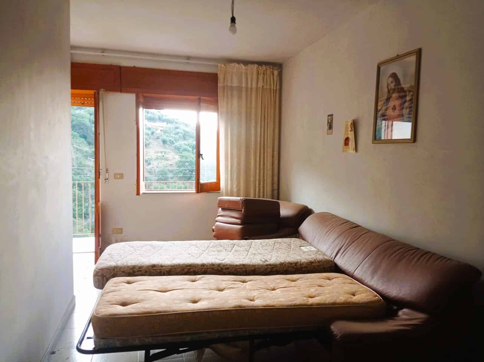Letto singolo e divano letto in appartamento con luce naturale e vista sul verde, arredato in stile classico, ideale per affitti turistici o residenziali.