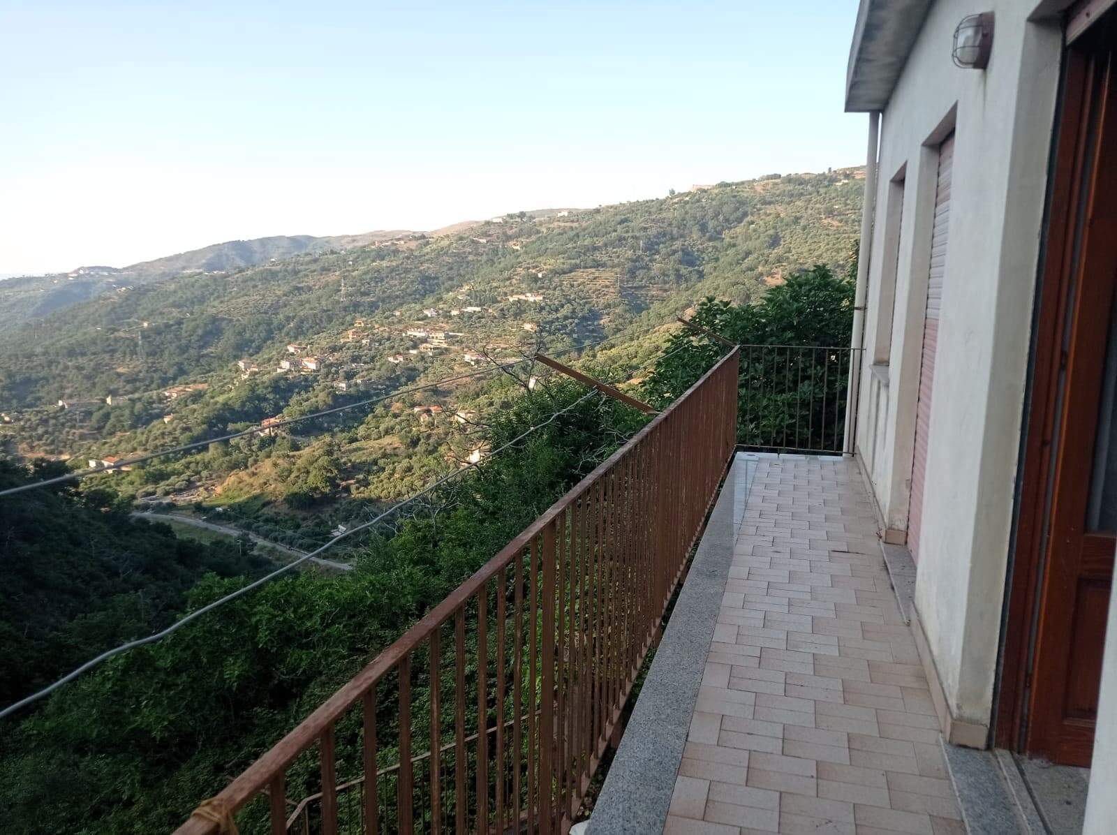Vista panoramica sulla campagna e le colline dal balcone di una casa in collina in Italia, con una ringhiera in ferro e un pavimento in piastrelle, perfetta per chi cerca immobili con vista naturale.