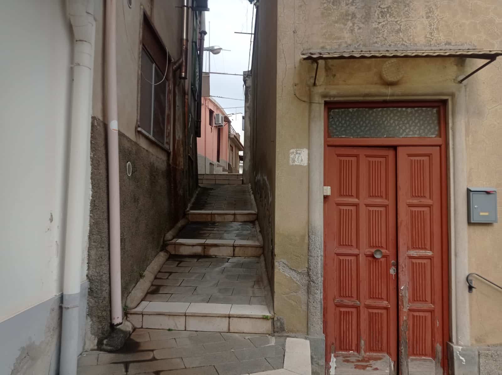 Scala esterna e portone d'ingresso di un appartamento in un vicolo storico, caratteristiche di case tipiche in Italia, con attenzione a dettagli come le scale in pietra e la porta di legno rossa.