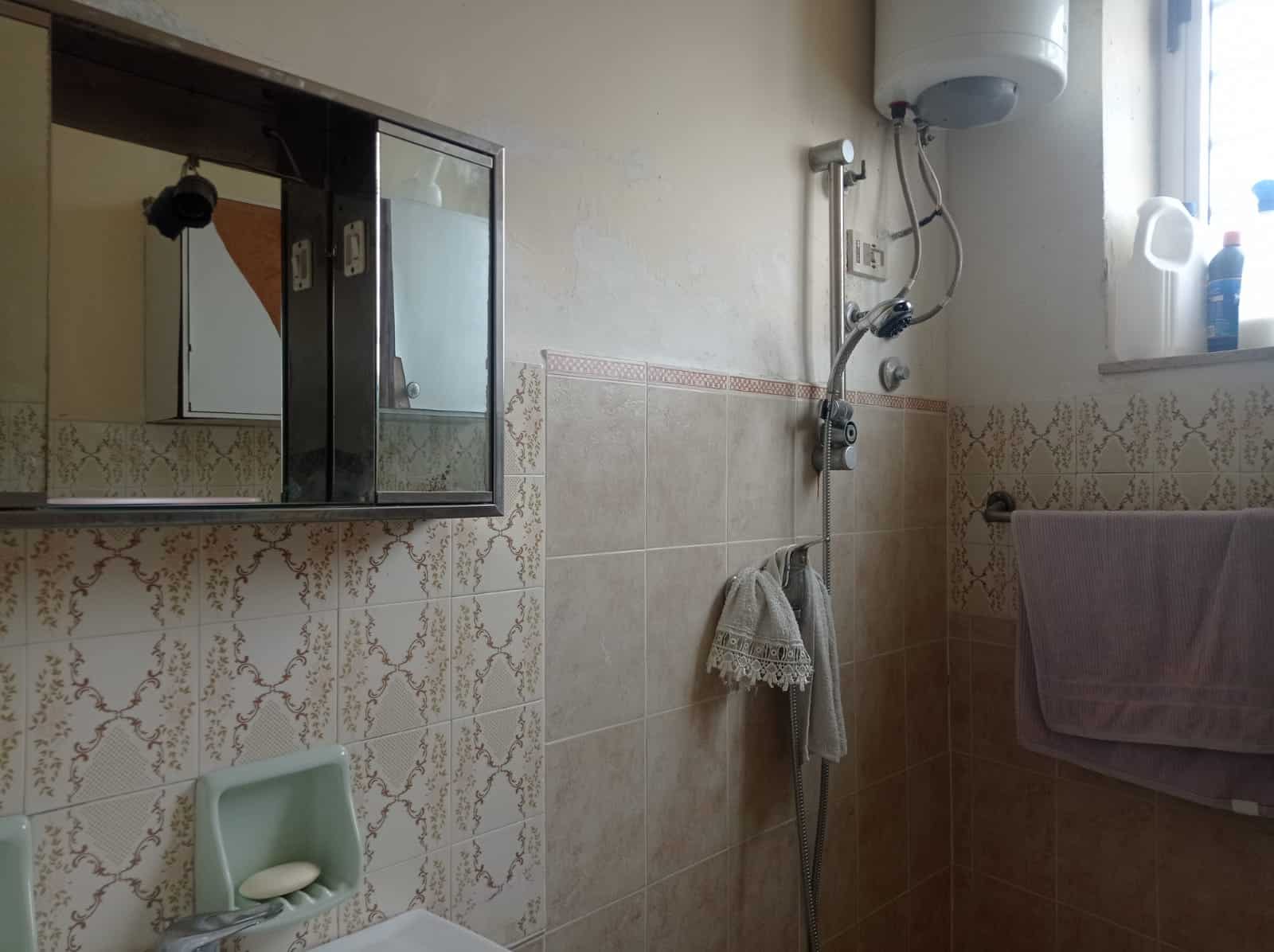 Vasca da bagno con doccia e specchio a muro in bagno, arredi pratici, rivestimenti in piastrelle beige e dettagli funzionali per il comfort quotidiano.