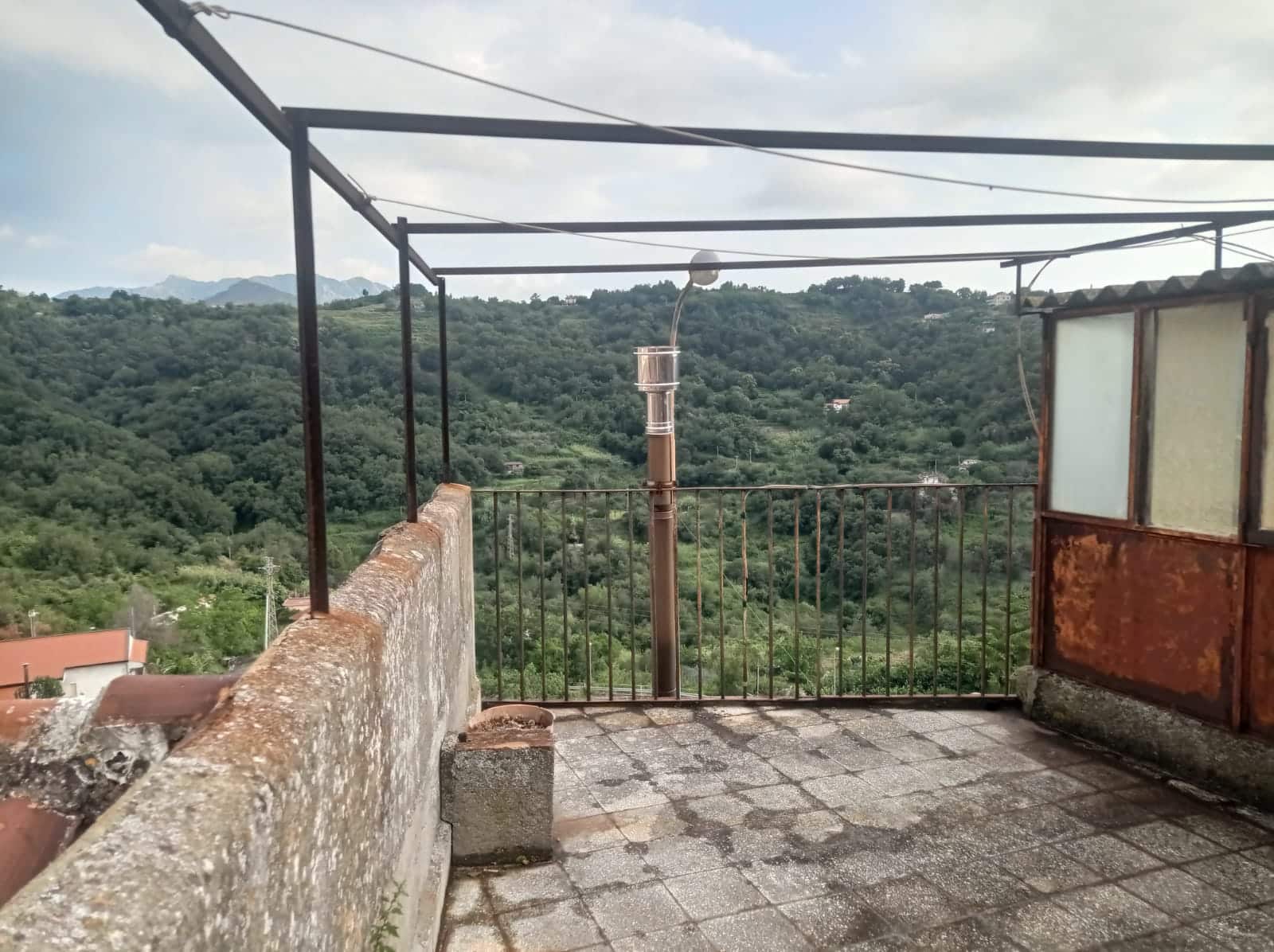 Balcone con vista panoramica sulle colline verdi e montagne, spazio esterno con ringhiera di ferro e pavimentazione in pietra, ambiente rustico e tranquillo, ideale per relax e godersi il paesaggio.