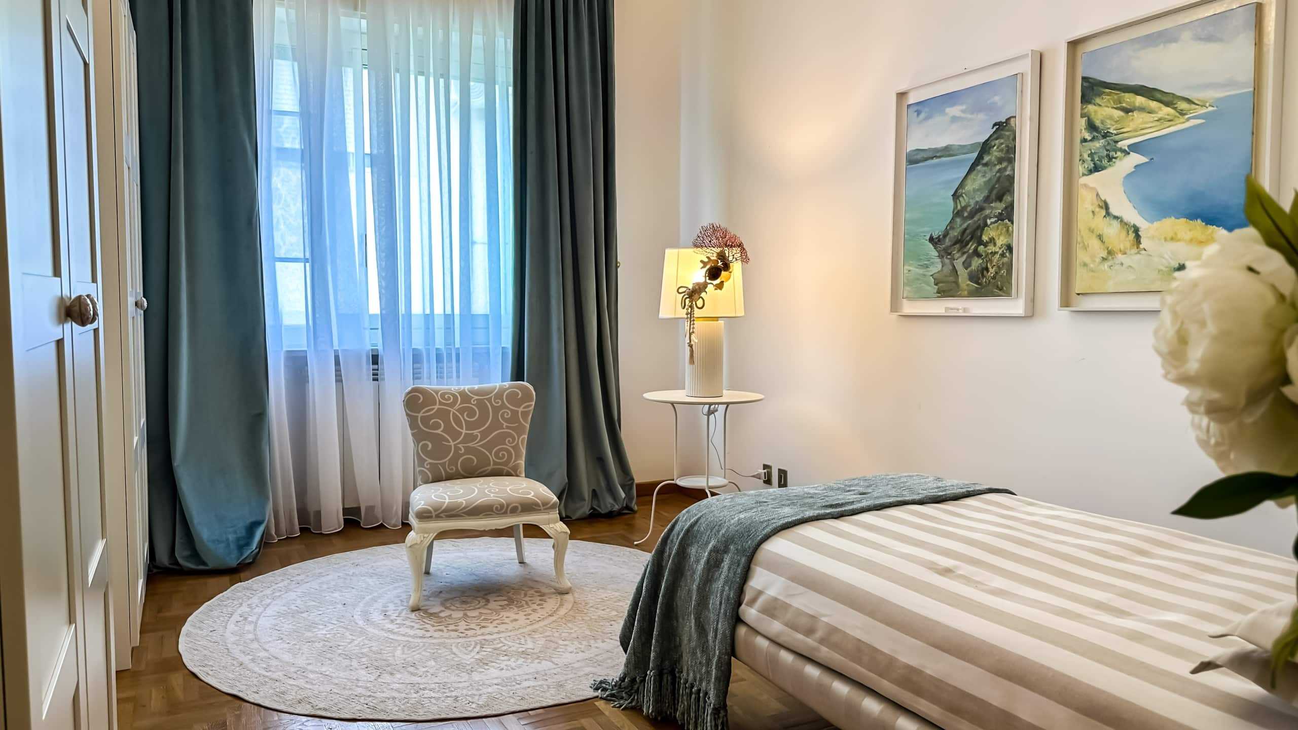 Camera da letto elegante con tende blu e quadri paesaggistici, arredamento raffinato, aria di comfort e relax, ideale per l'appartamento NextCasa.