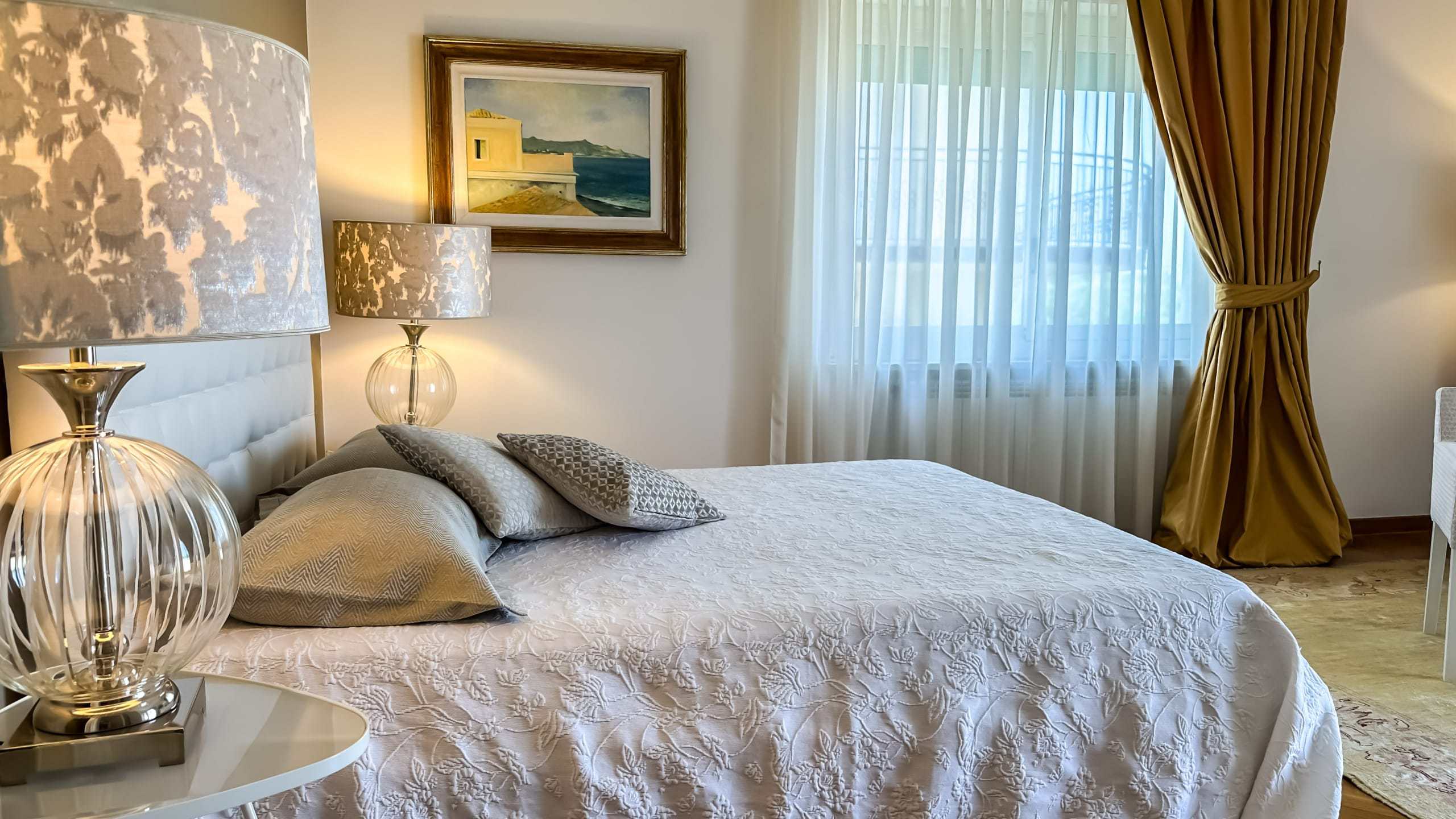 Immagine di una camera da letto elegante con letto matrimoniale, tende dorate, lampade di design e quadri decorativi, perfetta per soggiorni di lusso e comfort.