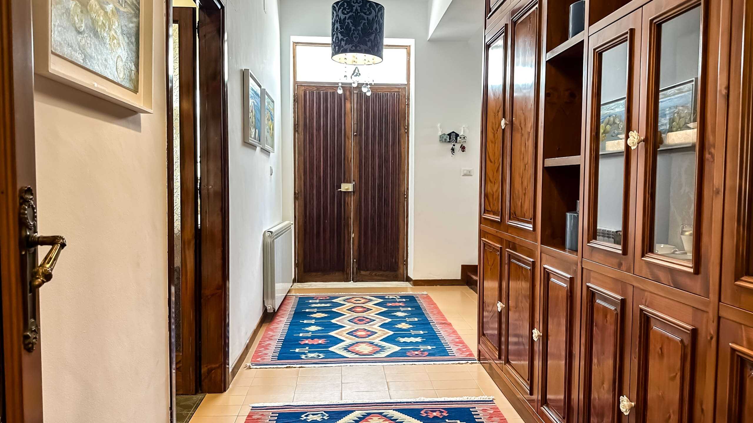 Porta di ingresso in legno, area armadio con mobili in stile classico, tappeto decorativo rustico, interno accogliente e caloroso, arredamento tradizionale, casa rustica e di charme, NextCasa.