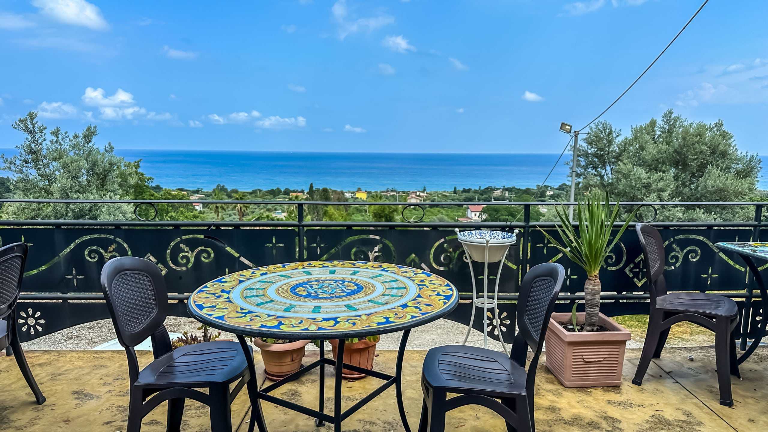 VISTA MARE DA BALCONE CON TAVOLINO IN CERAMICA, sedie nere e piante tropicali, panoramica su mare e paesaggi, ideale per affitto appartamenti NextCasa Italia.