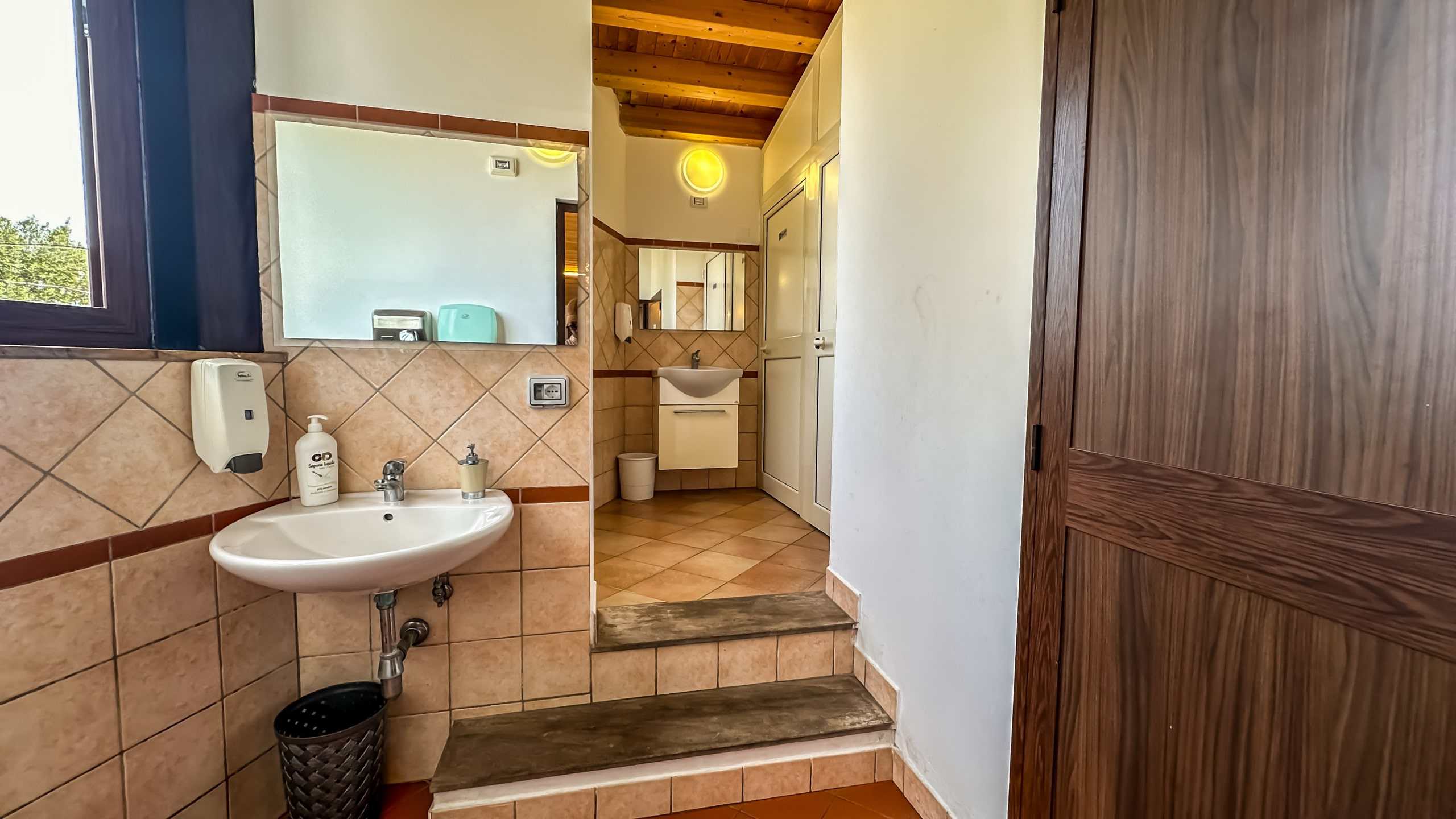 Lavabo e bagno in stile semplice e funzionale, con ante in legno e tessuti di ceramica beige, pratico per ambienti di case o strutture ricettive.