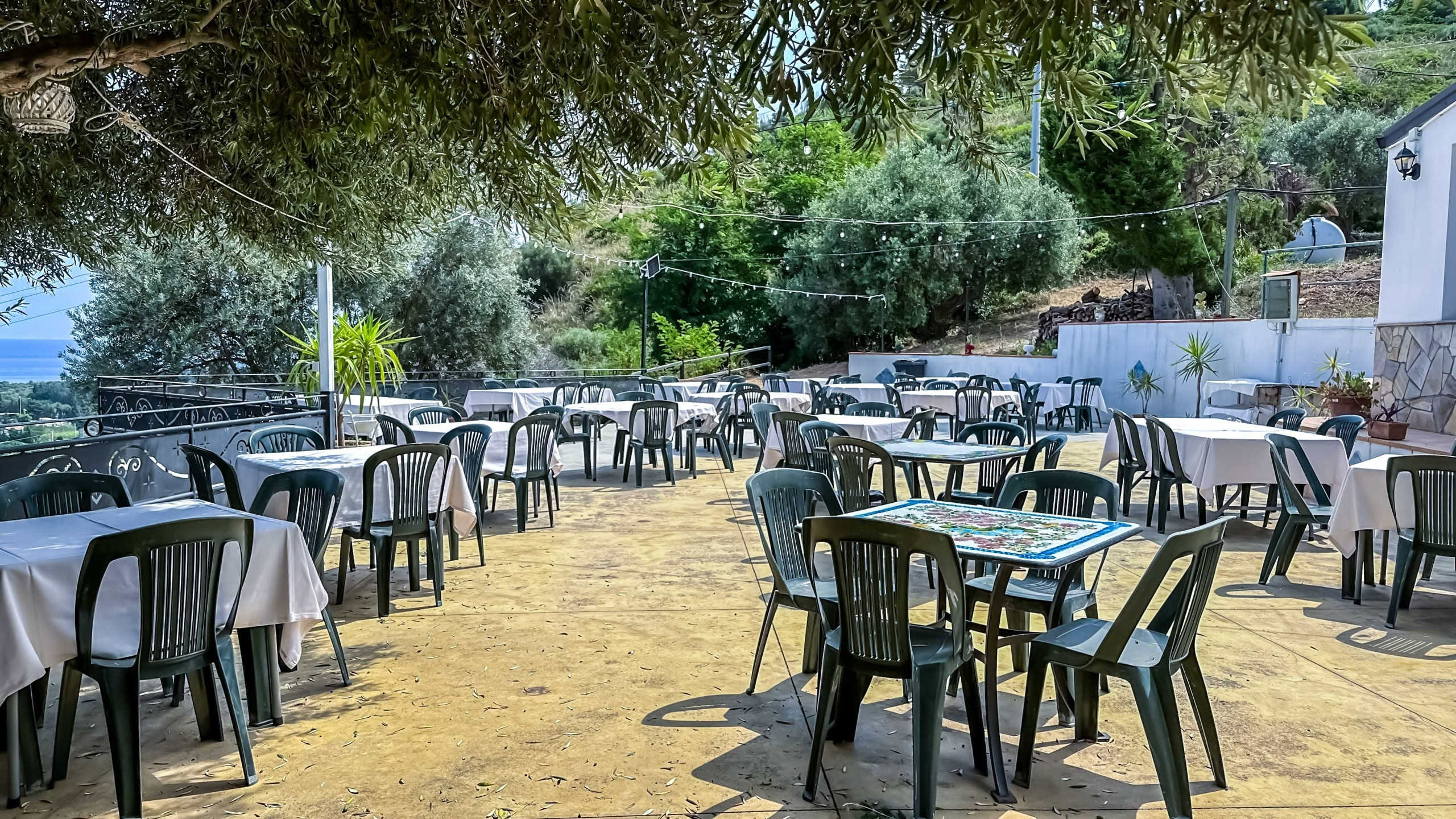 Ristorante all'aperto con tavoli e sedie in plastica, atmosfera rilassante e immersa nel verde, perfetto per pranzi estivi all'aperto con vista panoramica su natura e paesaggi italiani, ambiente conviviali e accogliente.